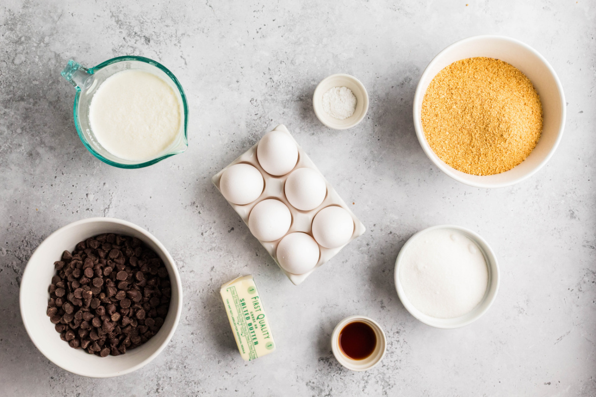 Ingredients for s'mores pie including graham cracker crumbs, chocolate chips, heavy cream, eggs, butter, sugar, vanilla, and cream of tartar.