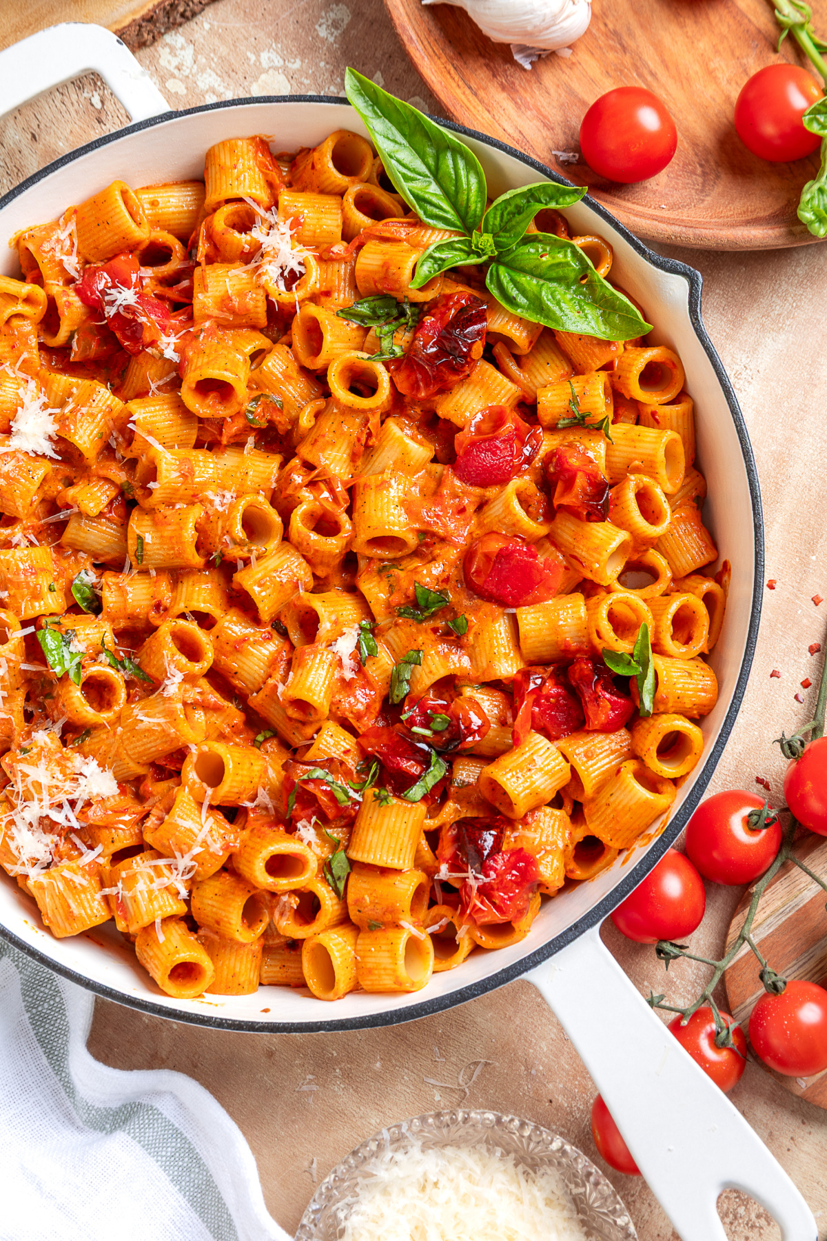 An overhead view of spicy roasted tomato vodka pasta with roasted grape tomatoes and fresh basil. Spicy roasted tomato vodka pasta topped with roasted grape tomatoes, fresh basil, and grated Parmesan in a white skillet.