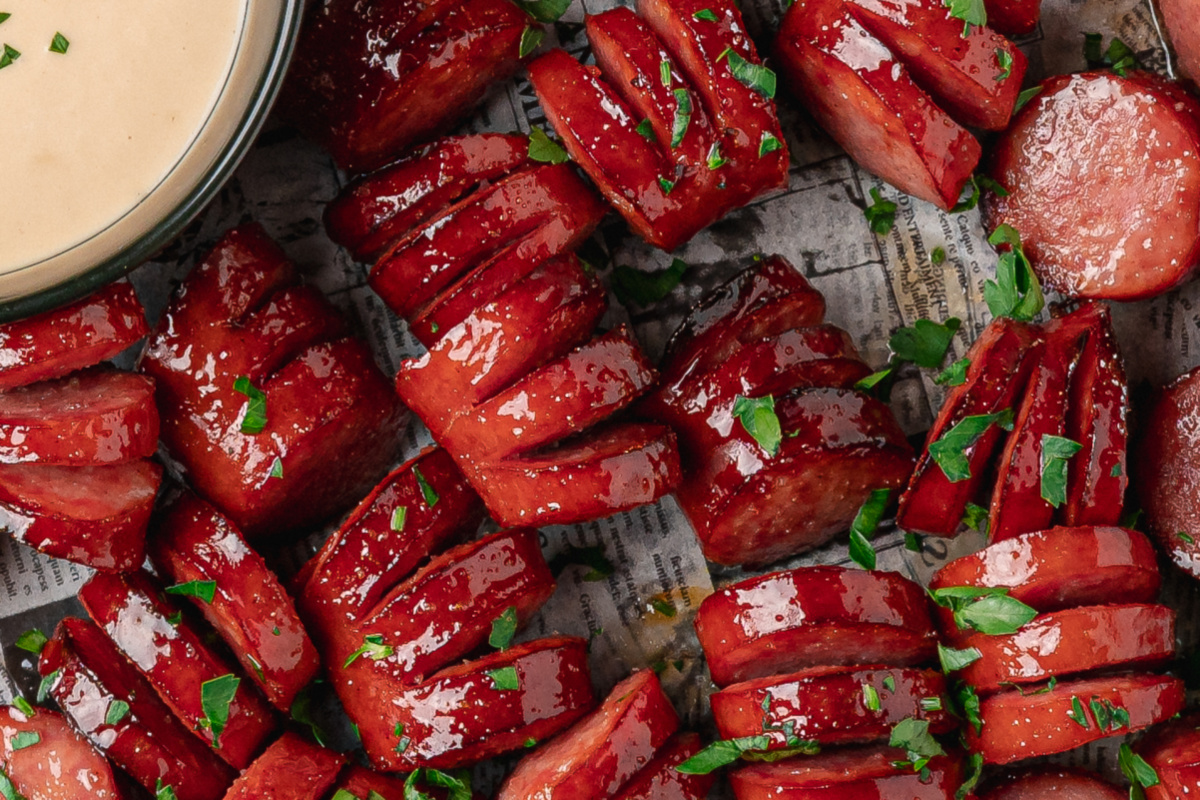 Close-up showing the glossy honey garlic glaze baked into the hasselback cuts. Close-up of sticky honey garlic kielbasa bites with glossy hasselback cuts.