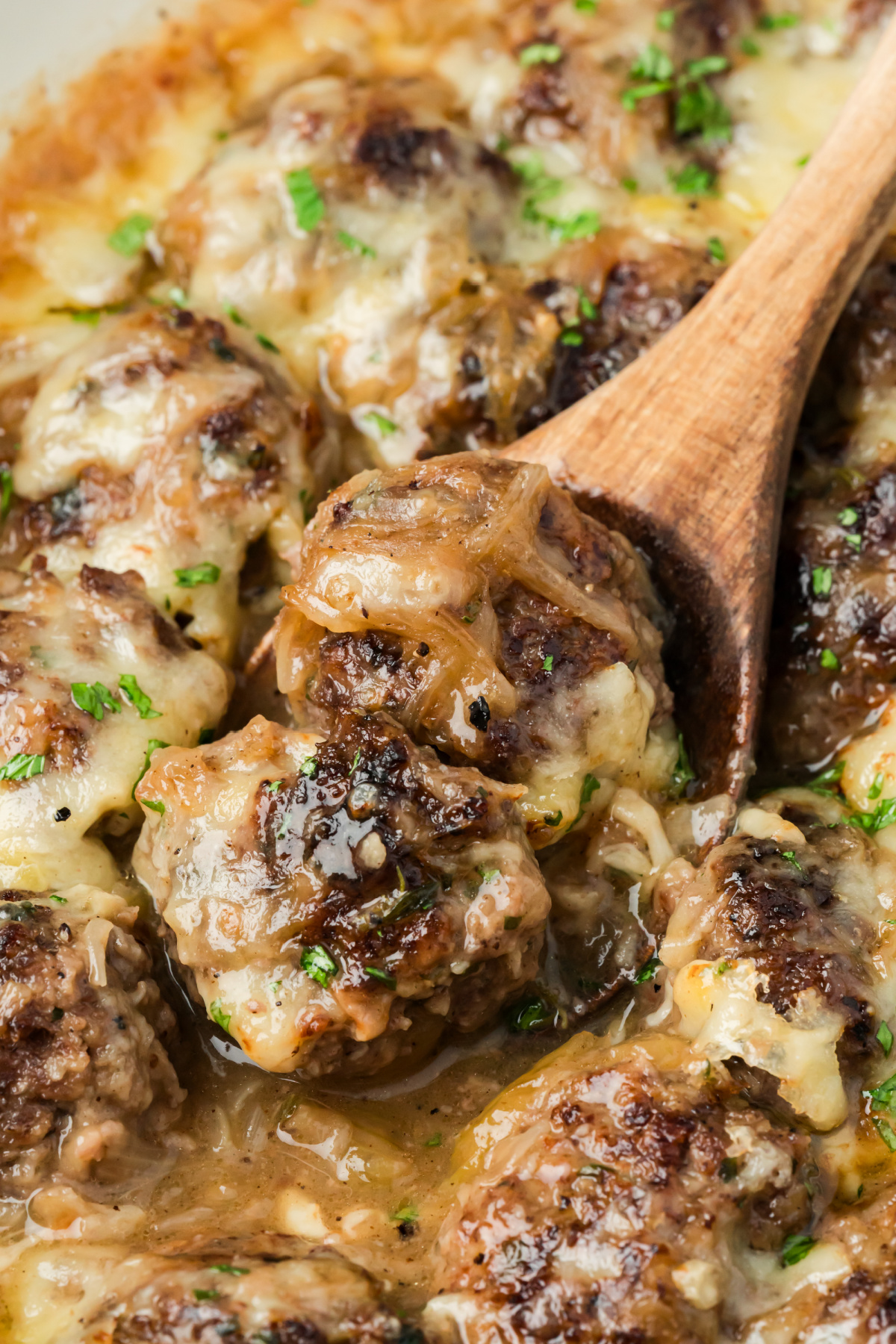 Caramelized onions and melted Gruyère cover browned beef meatballs in the skillet. Beef meatballs with caramelized onion sauce and melted Gruyère being served from the skillet