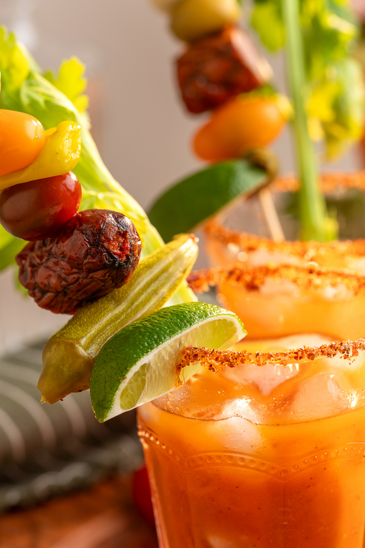 Close-up of a smoky Bloody Mary with a savory garnish skewer and Tajín rim Bloody Mary cocktail with a Tajín rim, celery, lime, pickled okra, tomatoes and smoked sausage garnish