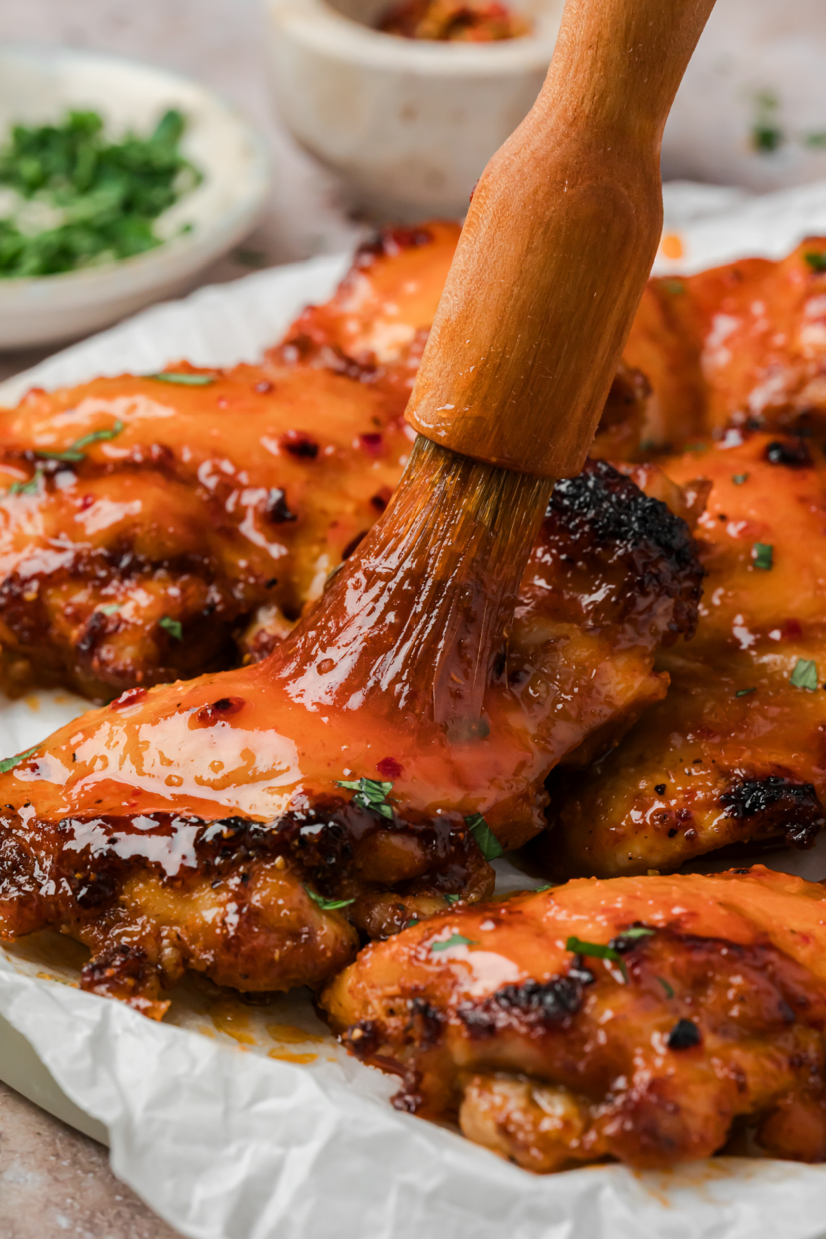 Brushing homemade hot honey glaze onto roasted chicken thighs before broiling.