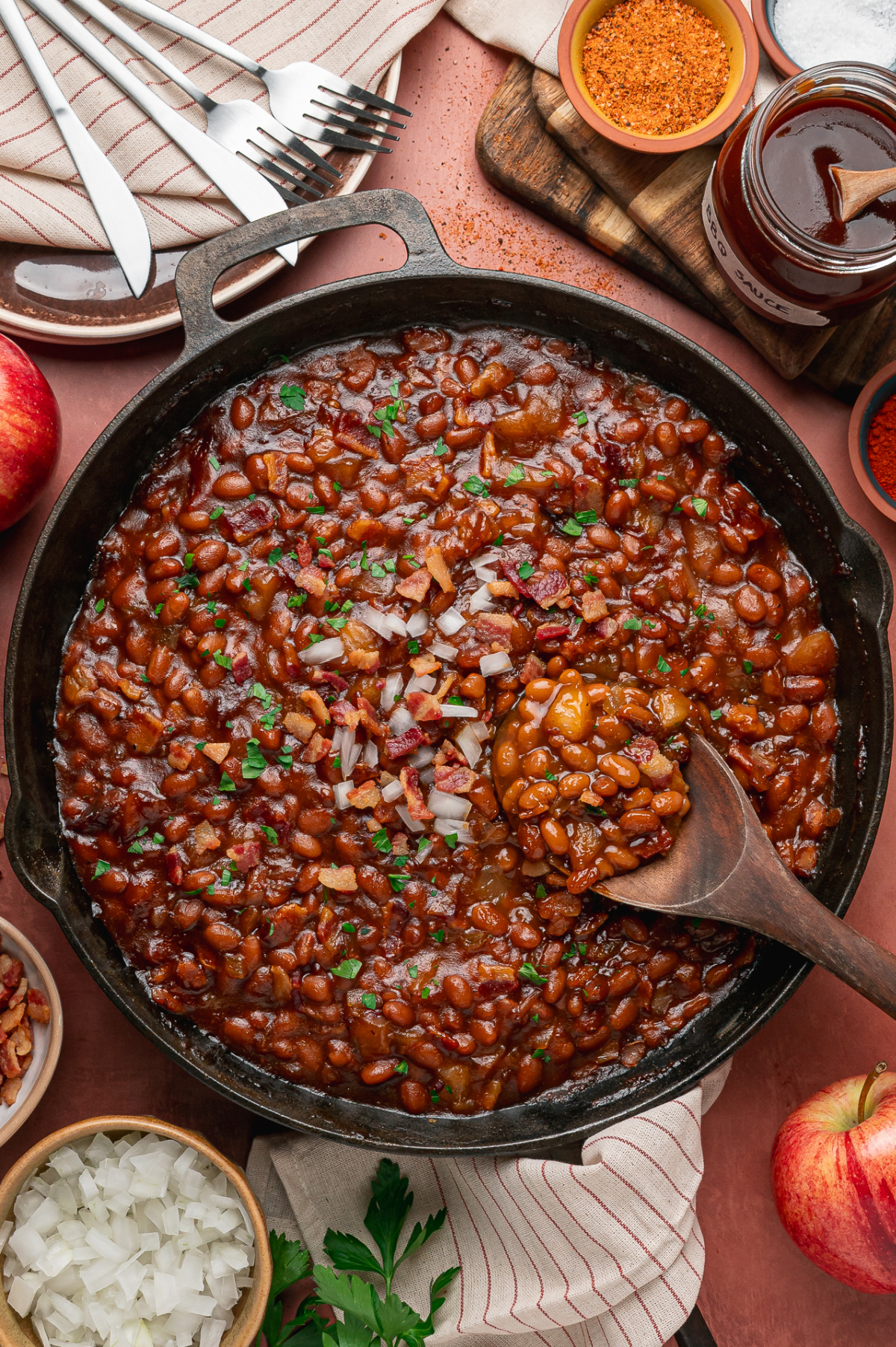 Cast-iron skillet of baked beans with apple pieces, bacon and smoky barbecue sauce