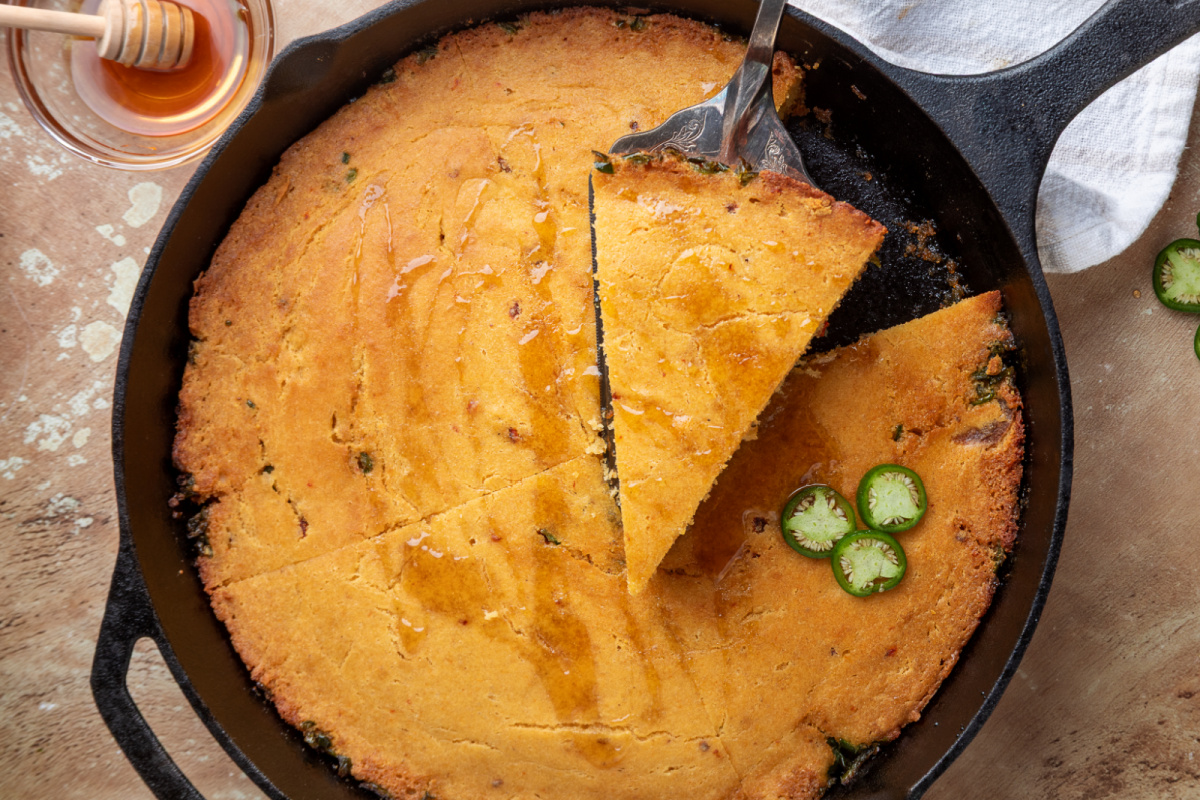 Cast-iron cornbread with smoky chipotle, fresh jalapeños and a hot honey finish Chipotle hot honey skillet cornbread sliced in a cast-iron skillet with hot honey drizzled over the top