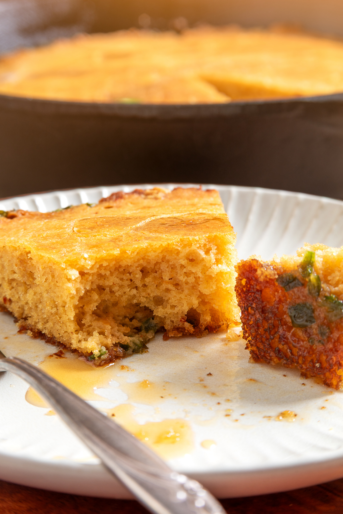 A slice of chipotle cornbread with hot honey and fresh jalapeños baked in cast iron Chipotle hot honey skillet cornbread slice showing the tender interior and jalapeños baked along the bottom