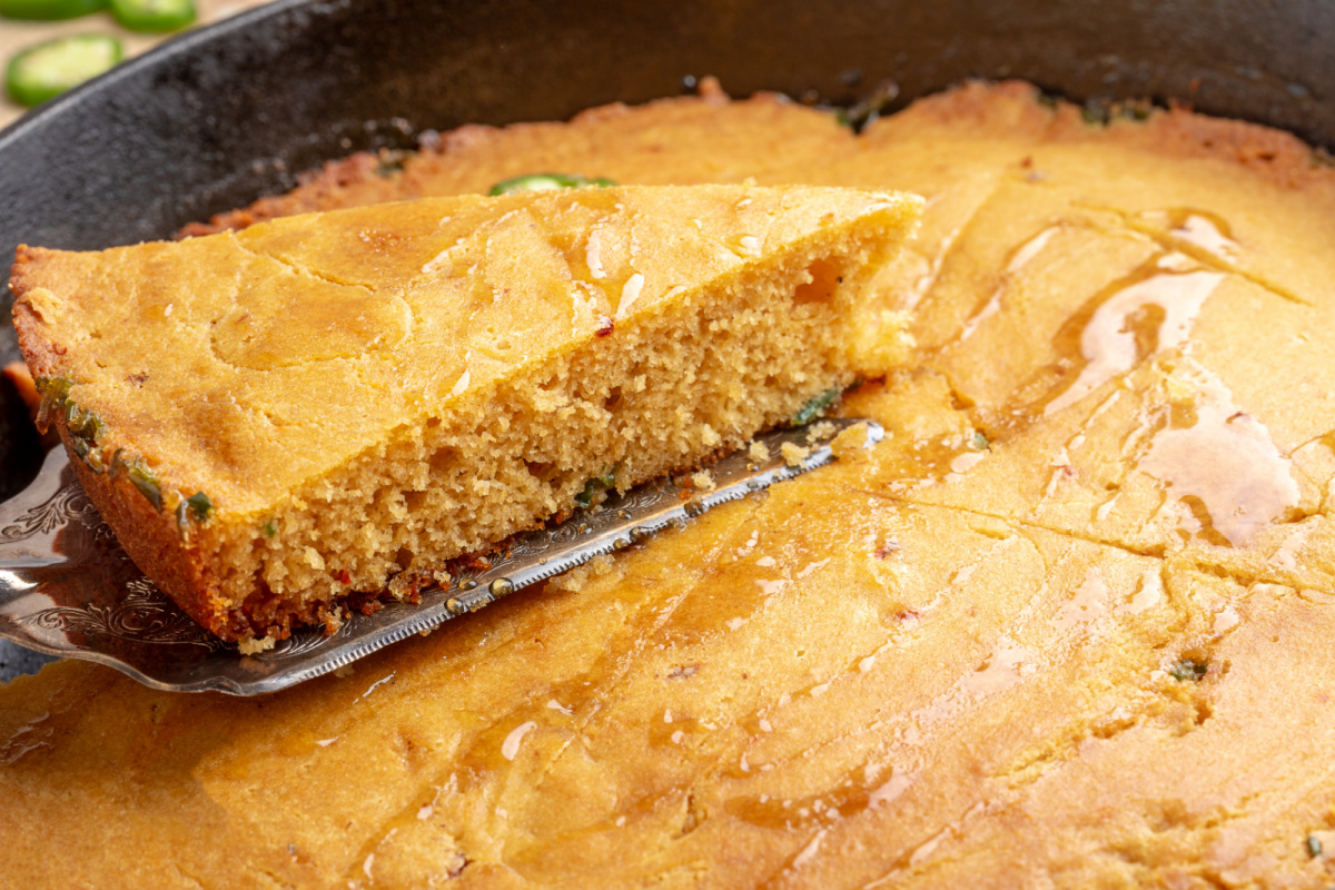 Tender chipotle cornbread with jalapeños and hot honey baked in a hot cast-iron skillet Slice of chipotle jalapeño cornbread lifted from a cast-iron skillet with hot honey drizzled over the top