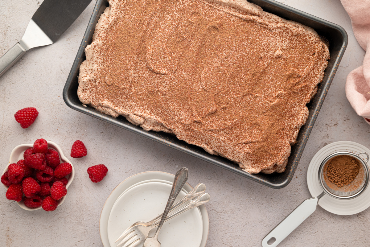 Chocolate whipped cream spread over the chilled tres leches cake. Pan of chocolate cake covered with chocolate whipped cream and a dusting of cocoa powder.