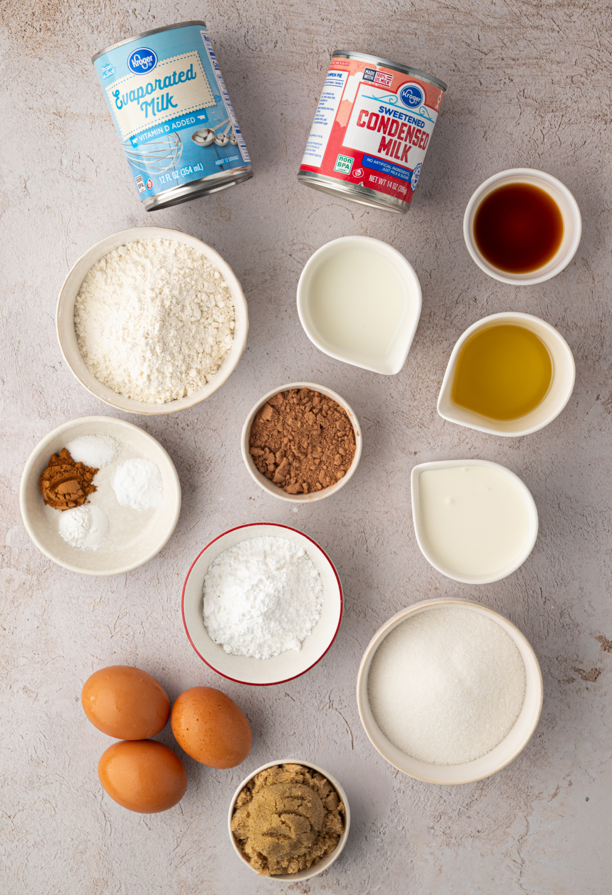 Ingredients for homemade chocolate tres leches cake with chocolate whipped cream. Ingredients for chocolate tres leches cake including cocoa powder, three milks, eggs, flour, sugar, oil, cinnamon, and vanilla.