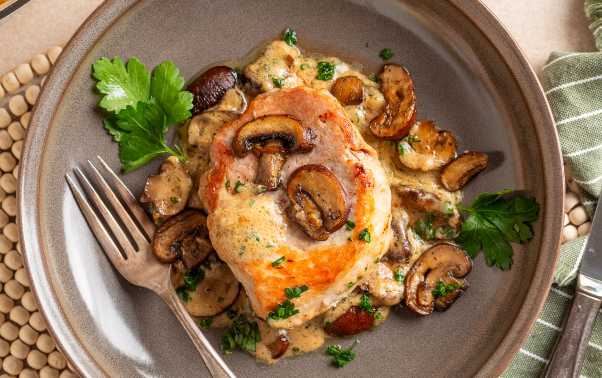Seared boneless pork chop plated with browned mushrooms, sage cream sauce and fresh parsley. Creamy mushroom pork chop served with roasted baby portobello mushrooms and sage cream sauce