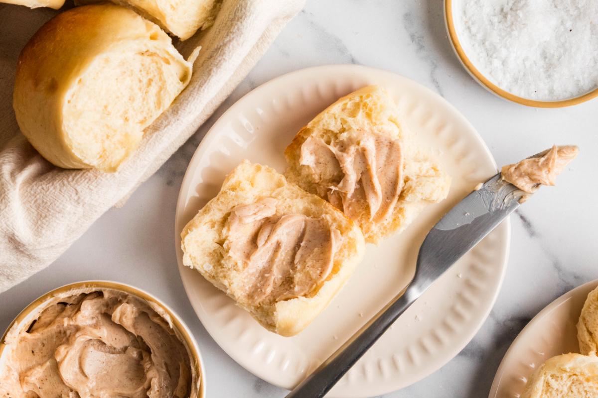 Split homemade dinner rolls spread with cinnamon maple butter on a plate.