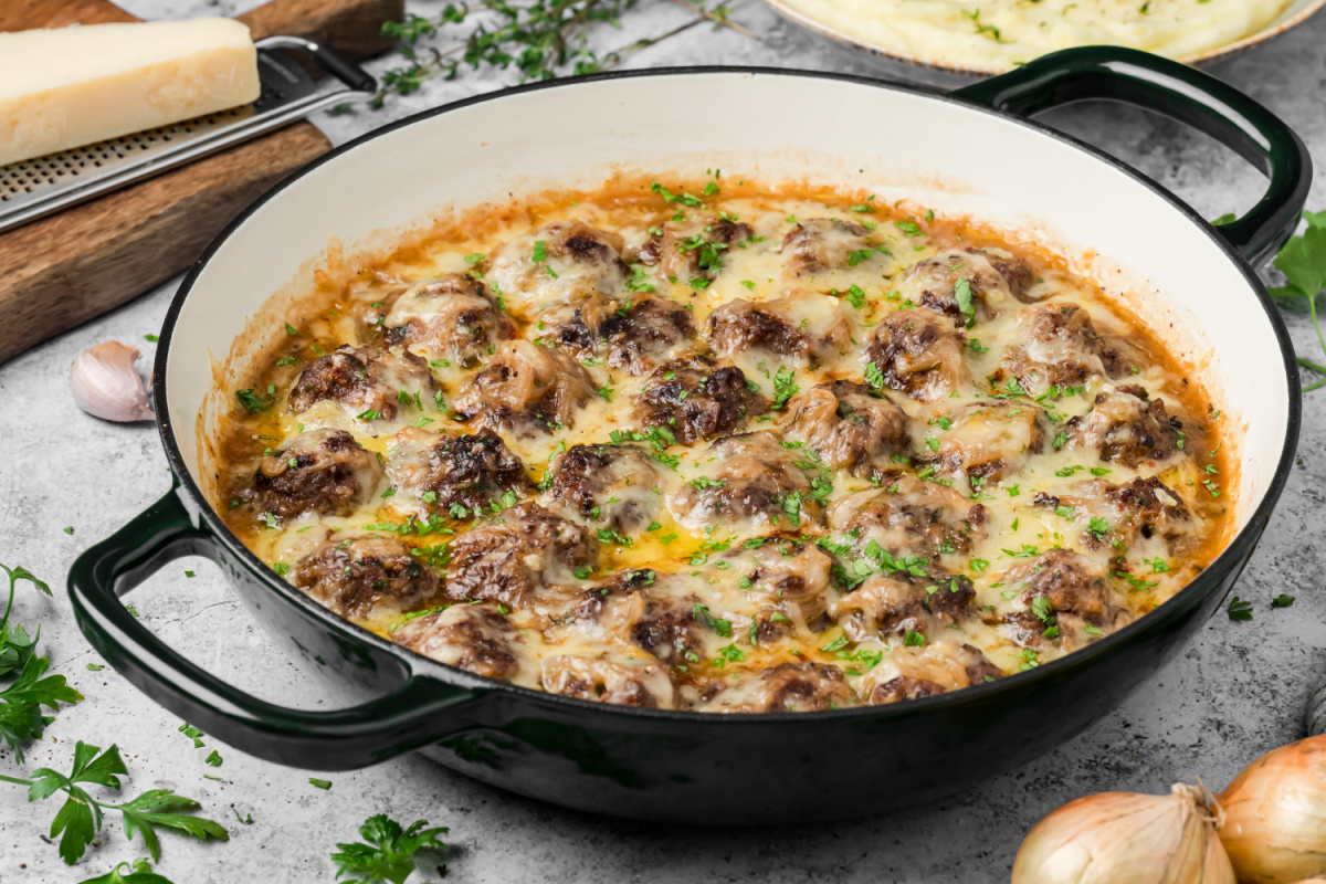 Skillet of French onion meatballs finished with caramelized onions, melted Gruyère and fresh parsley. French onion meatballs with caramelized onions and melted Gruyère in a skillet