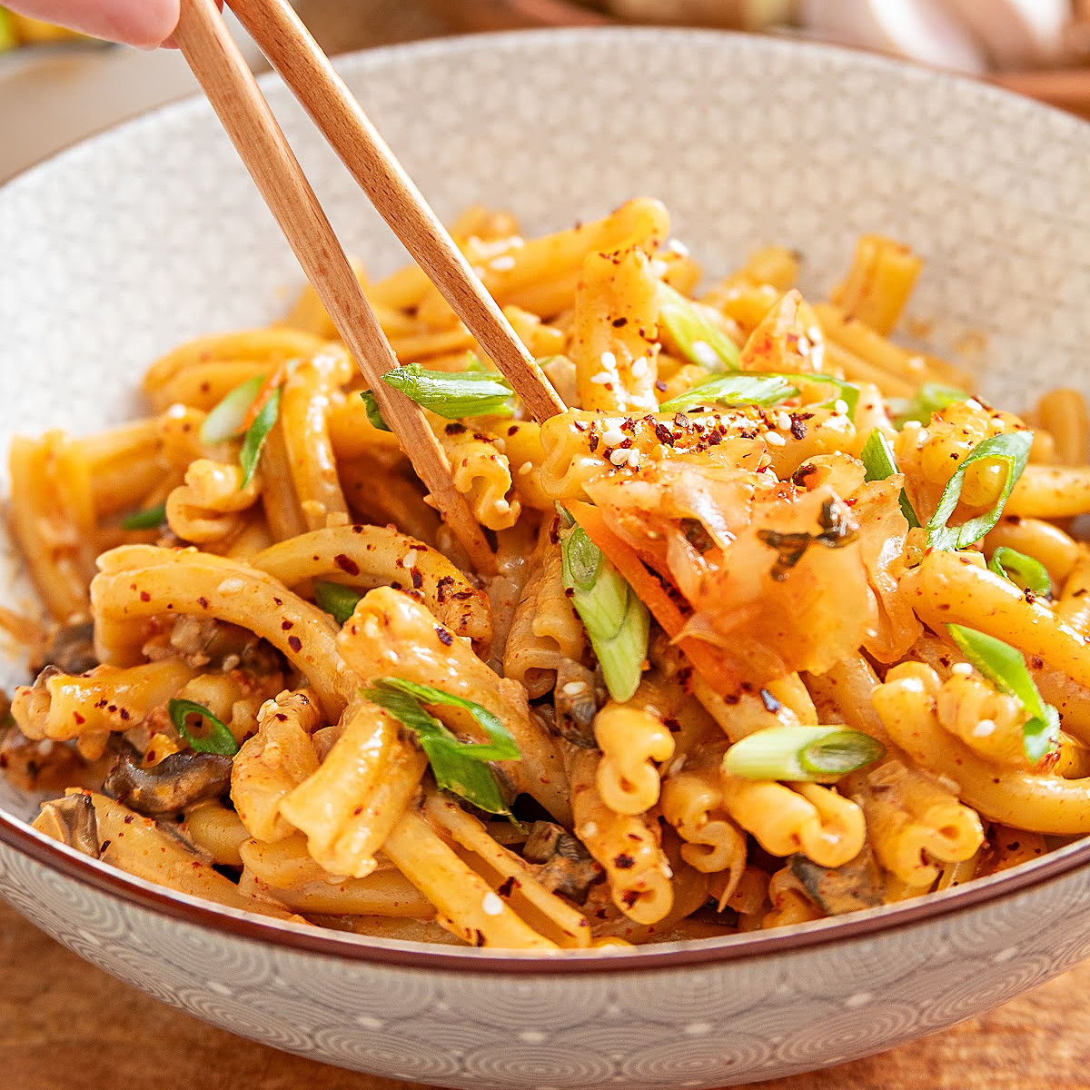 Gochujang pasta with mushrooms, kimchi, green onions and gochugaru lifted with chopsticks