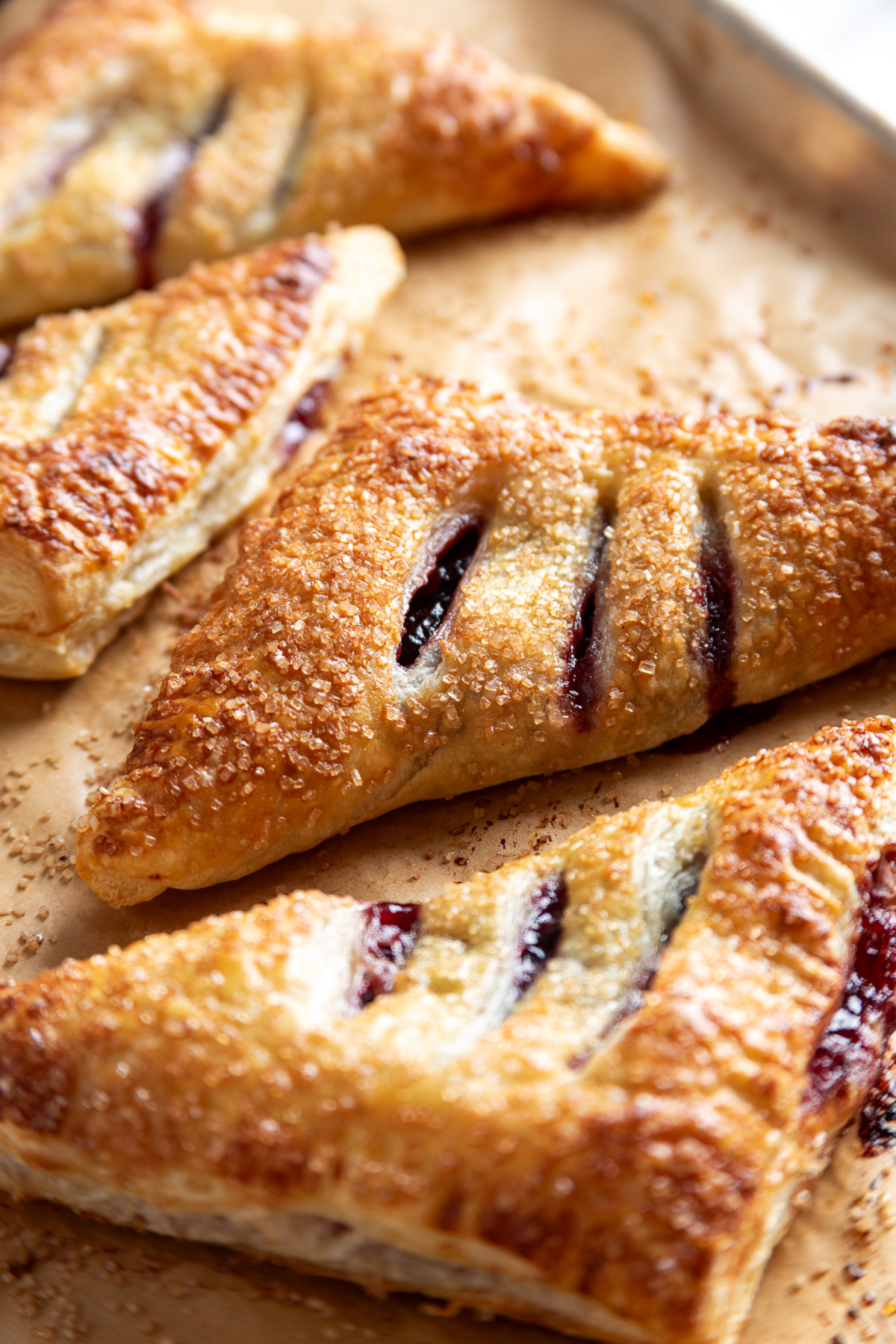 Freshly baked dark cherry puff pastry turnovers before glazing Golden puff pastry turnovers filled with dark cherries and topped with coarse sugar