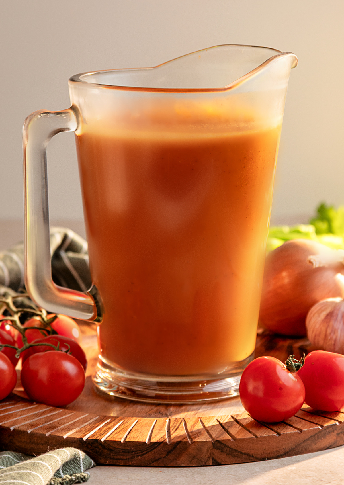 Pitcher of homemade Bloody Mary mix made with smoked Roma tomatoes and aromatics Homemade smoked Bloody Mary mix in a glass pitcher surrounded by fresh tomatoes, onion and garlic