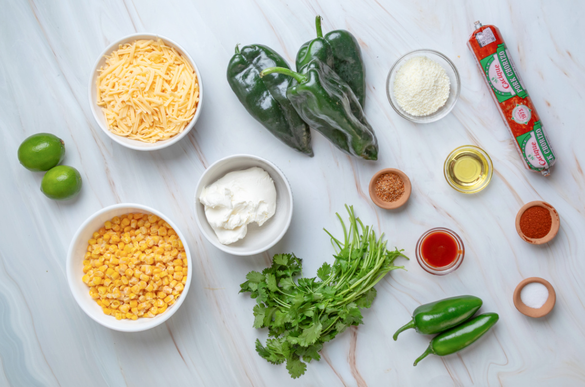 Ingredients for Mexican street corn stuffed poblano peppers including poblanos, corn, chorizo, cream cheese, shredded cheese, Cotija, jalape&ntilde;os, cilantro and lime