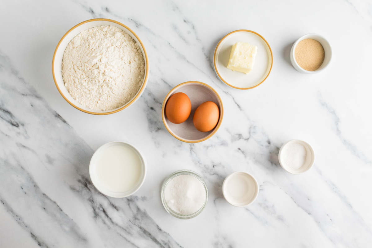 Ingredients for homemade milk bread rolls including bread flour, whole milk, eggs, butter, sugar, yeast and salt.