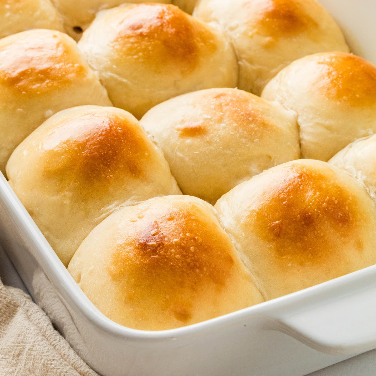 Soft milk bread rolls baked together in a white baking dish with golden brown tops and tender pull-apart sides.
