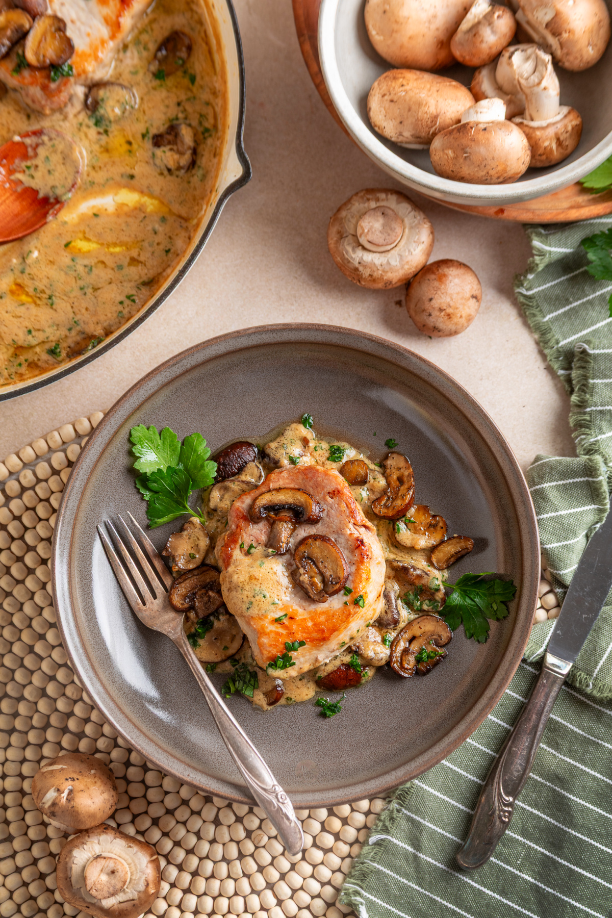 Seared pork chop served with roasted mushrooms and sage cream sauce, with baby portobellos alongside. Plated boneless pork chop with roasted baby portobello mushrooms and fresh sage cream sauce
