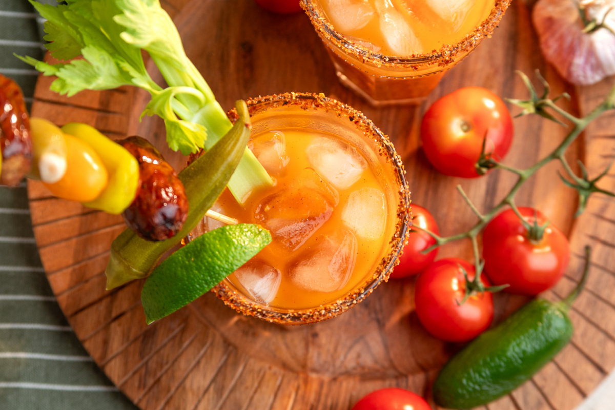 Bloody Mary made with smoked tomato mix and loaded with savory garnishes Smoked tomato Bloody Mary cocktail over ice with a Tajín rim, celery, lime, pickled okra and smoked sausage