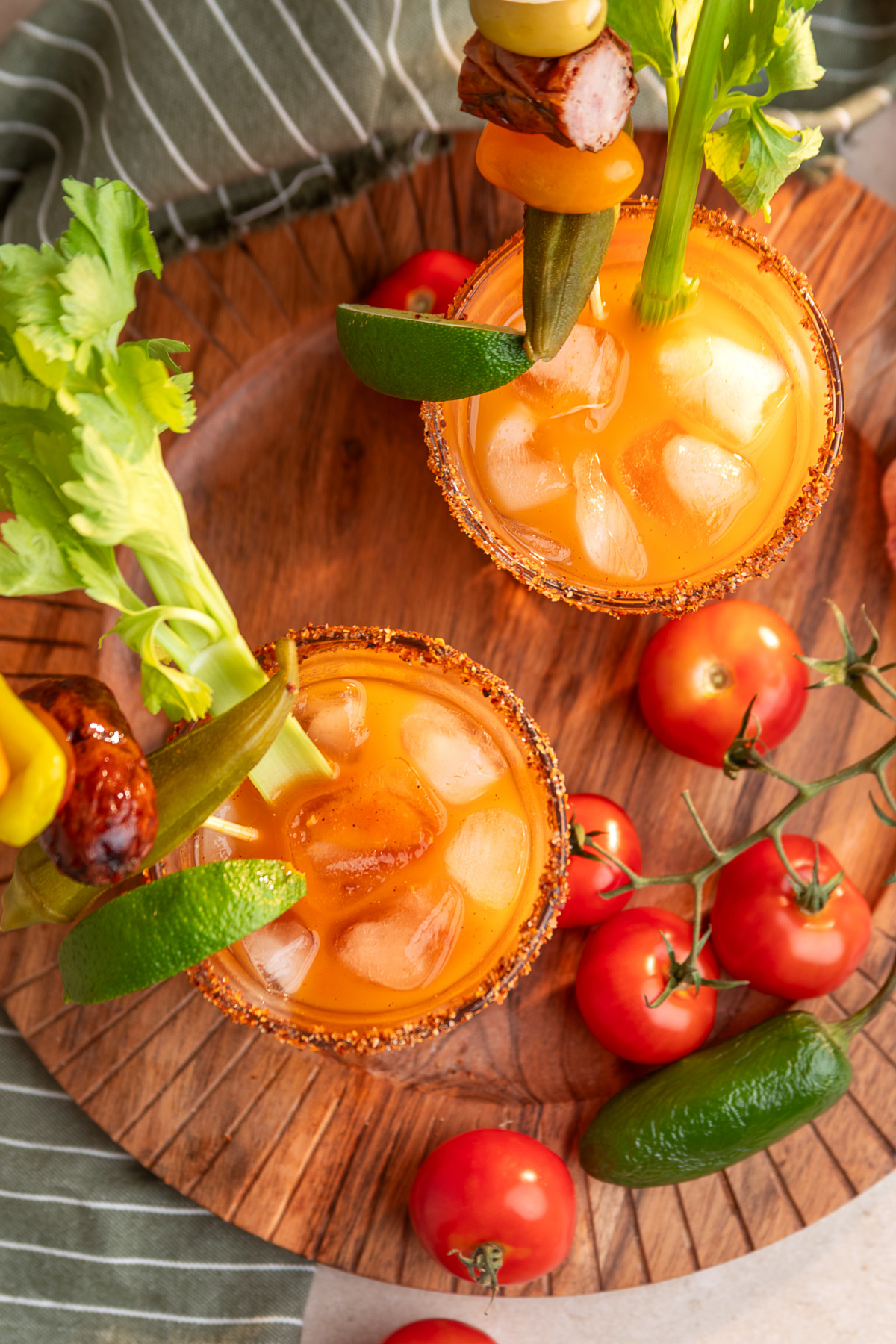 Bloody Mary cocktails over ice with celery and stacked savory garnish skewers Two smoked Bloody Mary cocktails with Tajín rims, celery, lime, pickled okra, smoked sausage and tomato garnishes