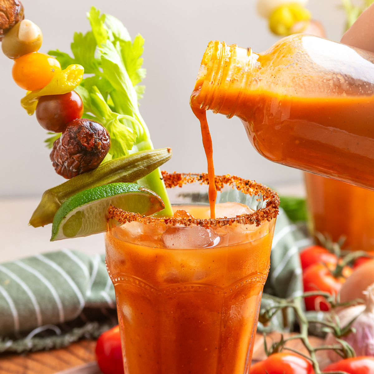Smoked tomato Bloody Mary mix poured into an ice-filled glass with celery, lime, pickled okra and smoked sausage