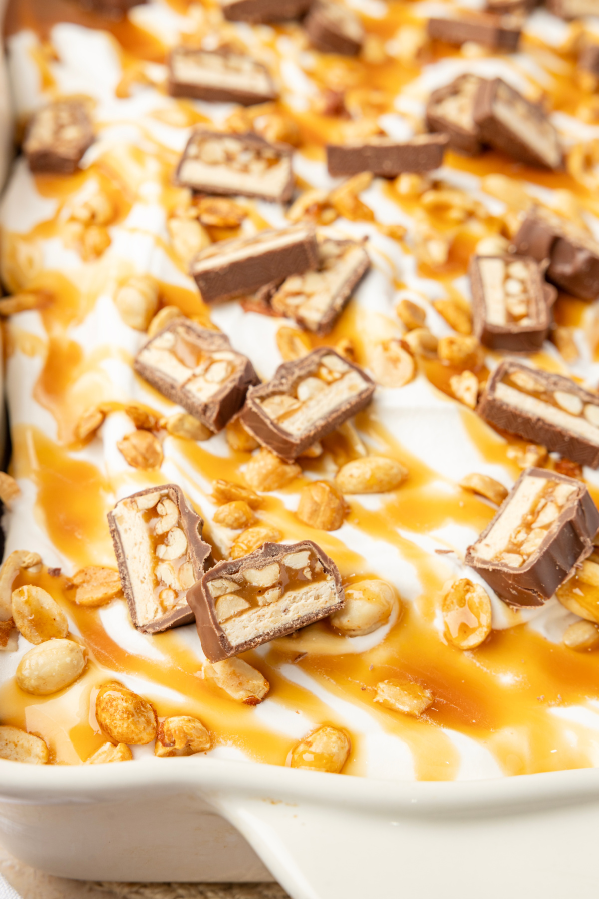 Close-up of chopped Snickers, salted peanuts and caramel over the whipped topping Chopped Snickers bars, caramel and roasted salted peanuts over whipped topping on chocolate cake