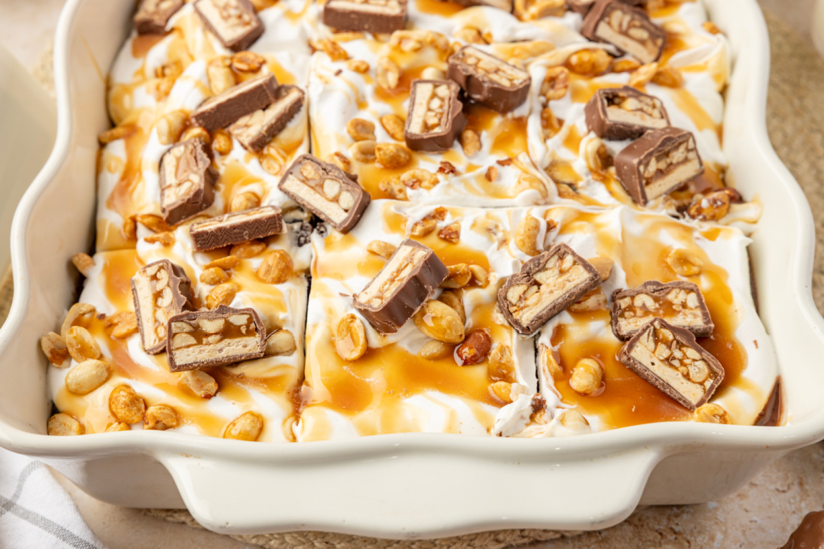 Finished chocolate poke cake covered with caramel, salted peanuts and chopped Snickers bars snickers-poke-cake-caramel-peanut-topping