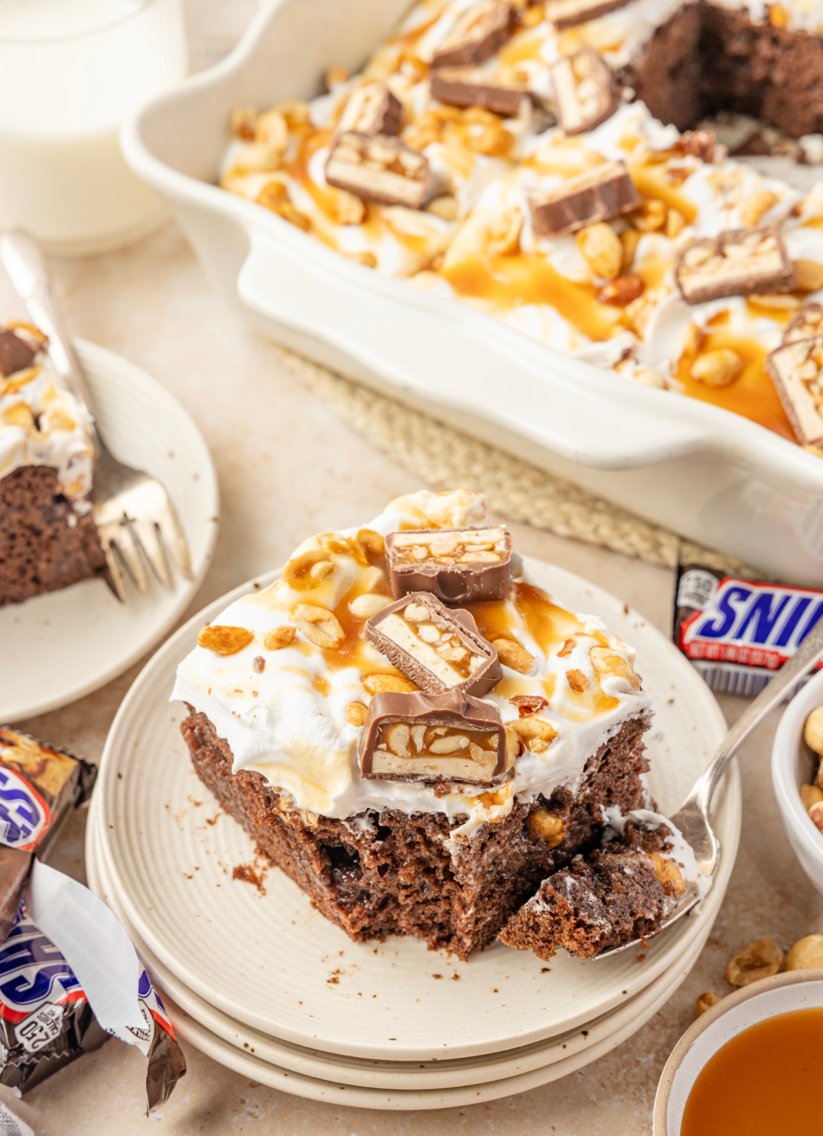 Chocolate pudding poke cake slice with caramel, roasted salted peanuts and chopped Snickers Snickers poke cake slice with chocolate pudding, caramel, salted peanuts and chopped candy bars
