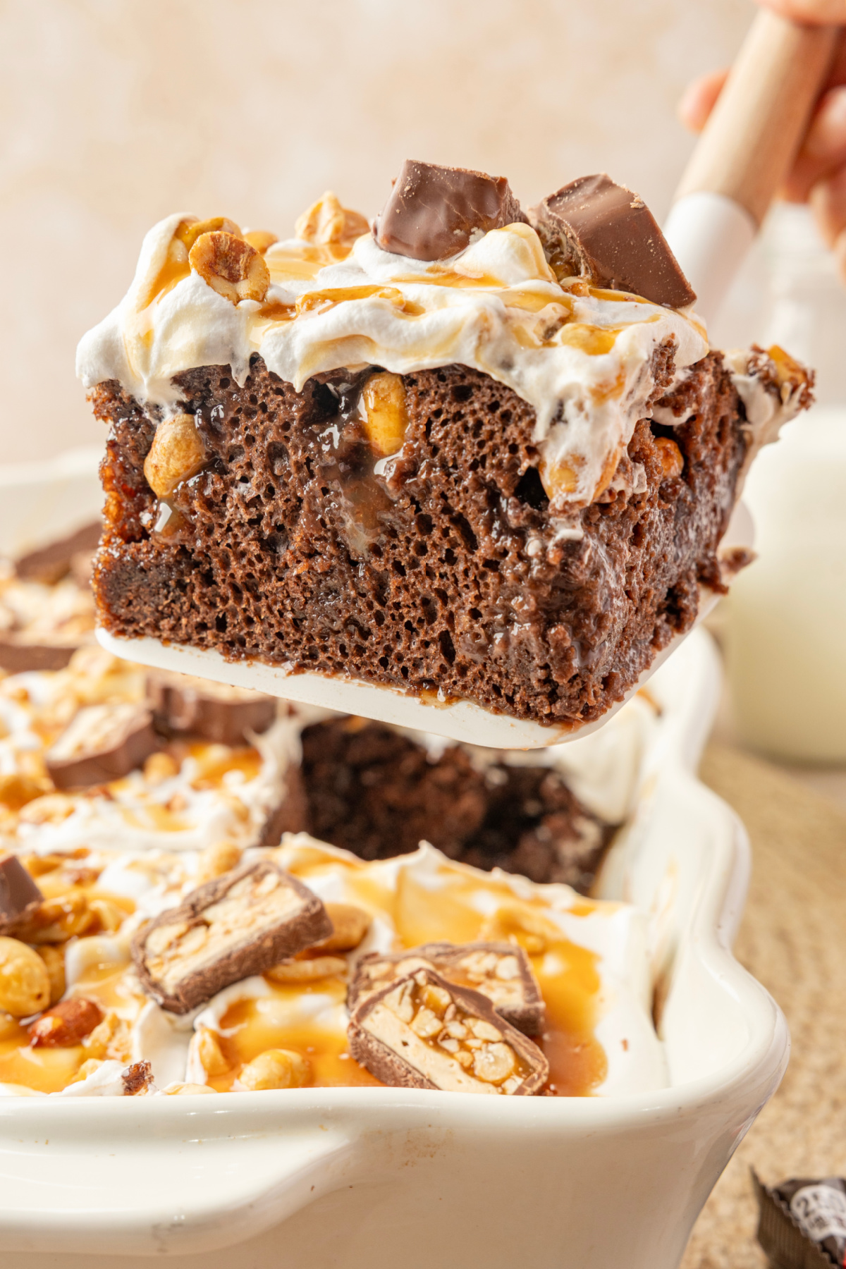 Snickers poke cake slice filled with chocolate pudding, caramel and roasted salted peanuts