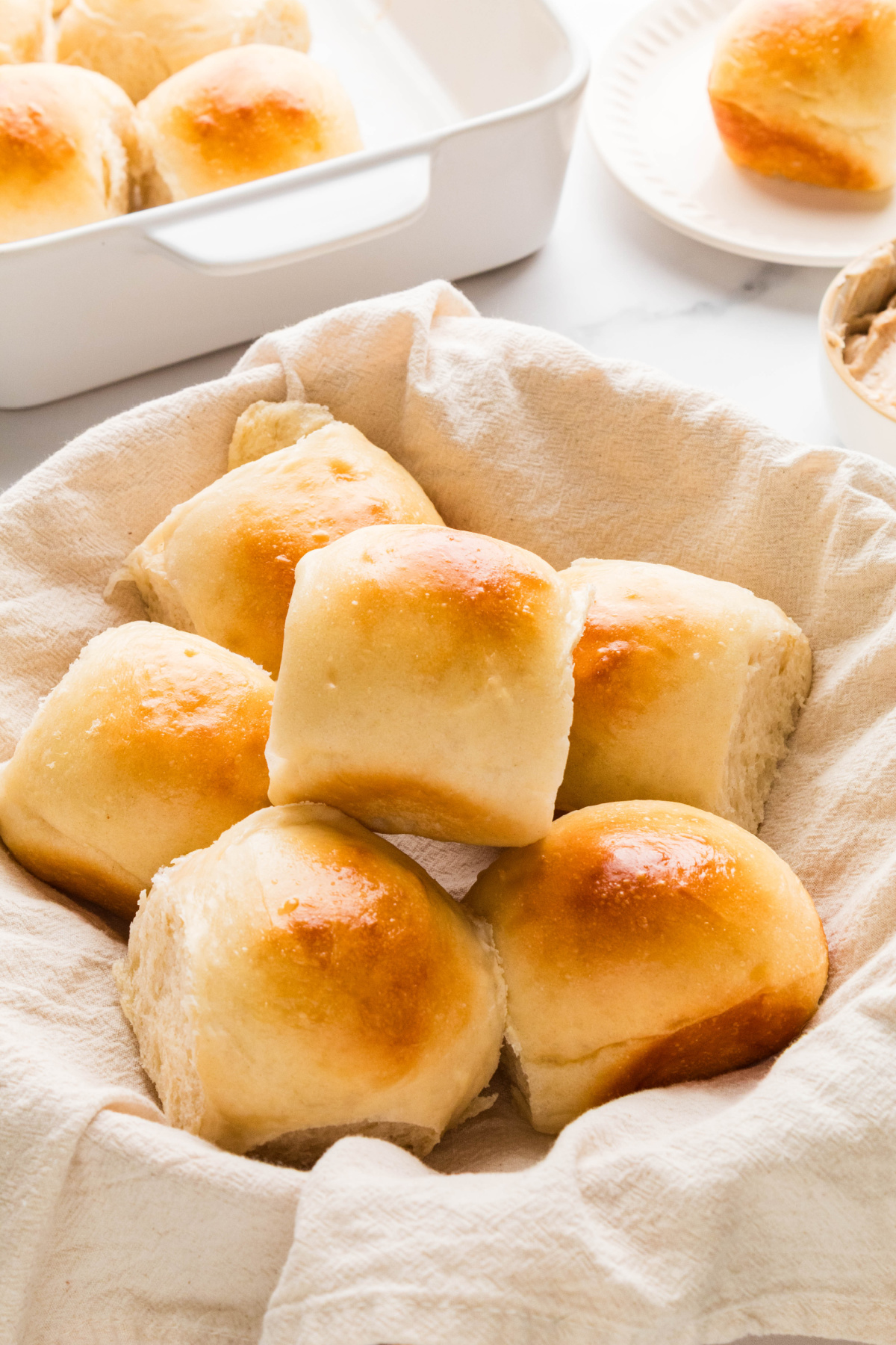 Soft golden dinner rolls arranged in a cloth-lined serving basket.