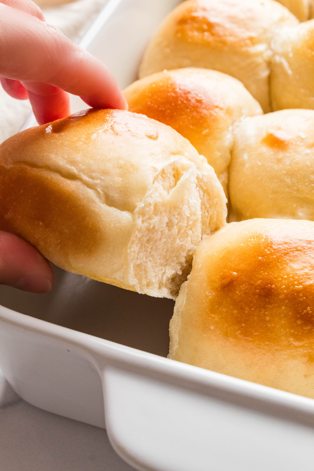 Hand pulling a soft dinner roll from the baking dish to reveal its tender interior.