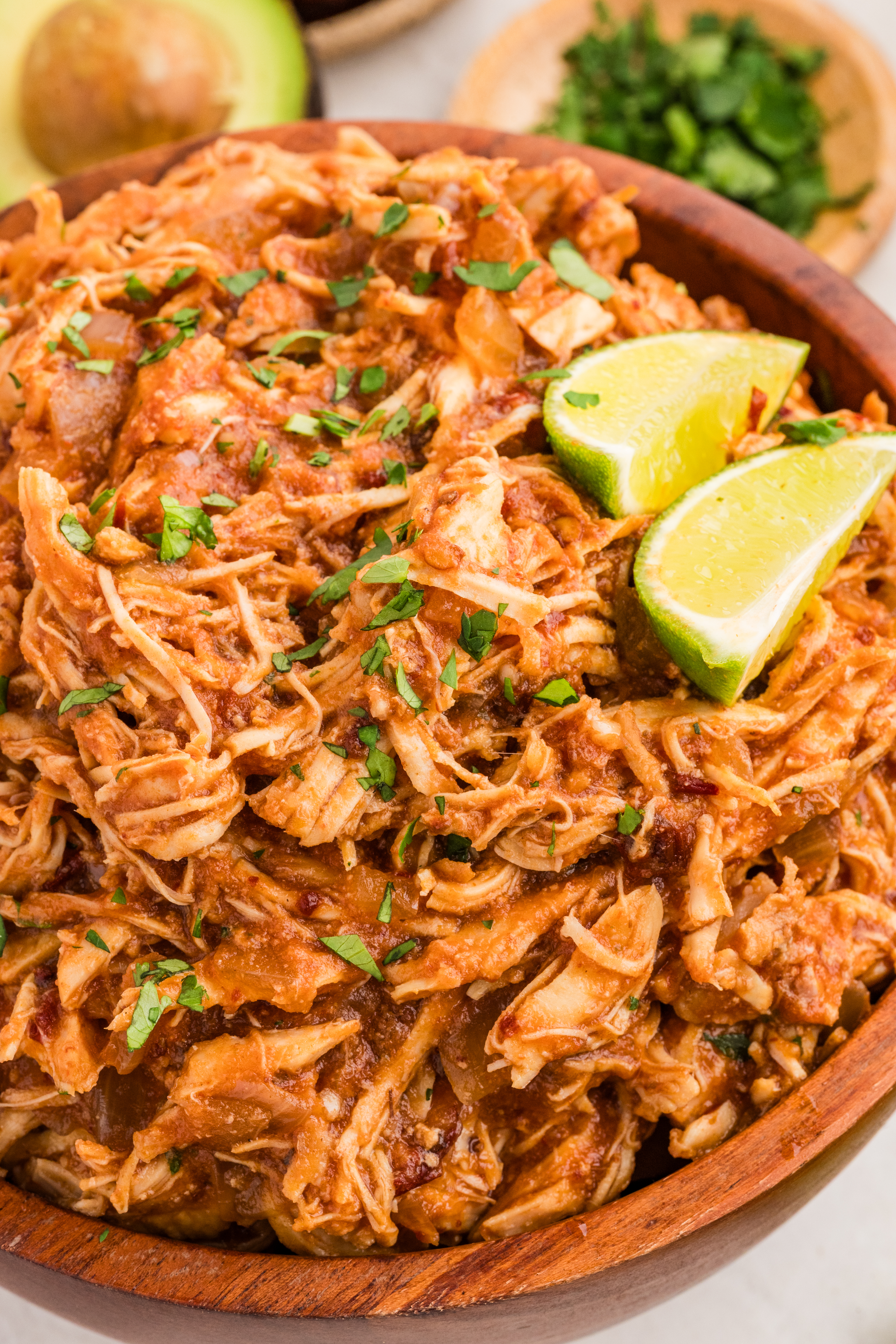 Shredded chipotle chicken in a wooden bowl topped with cilantro and fresh lime wedges