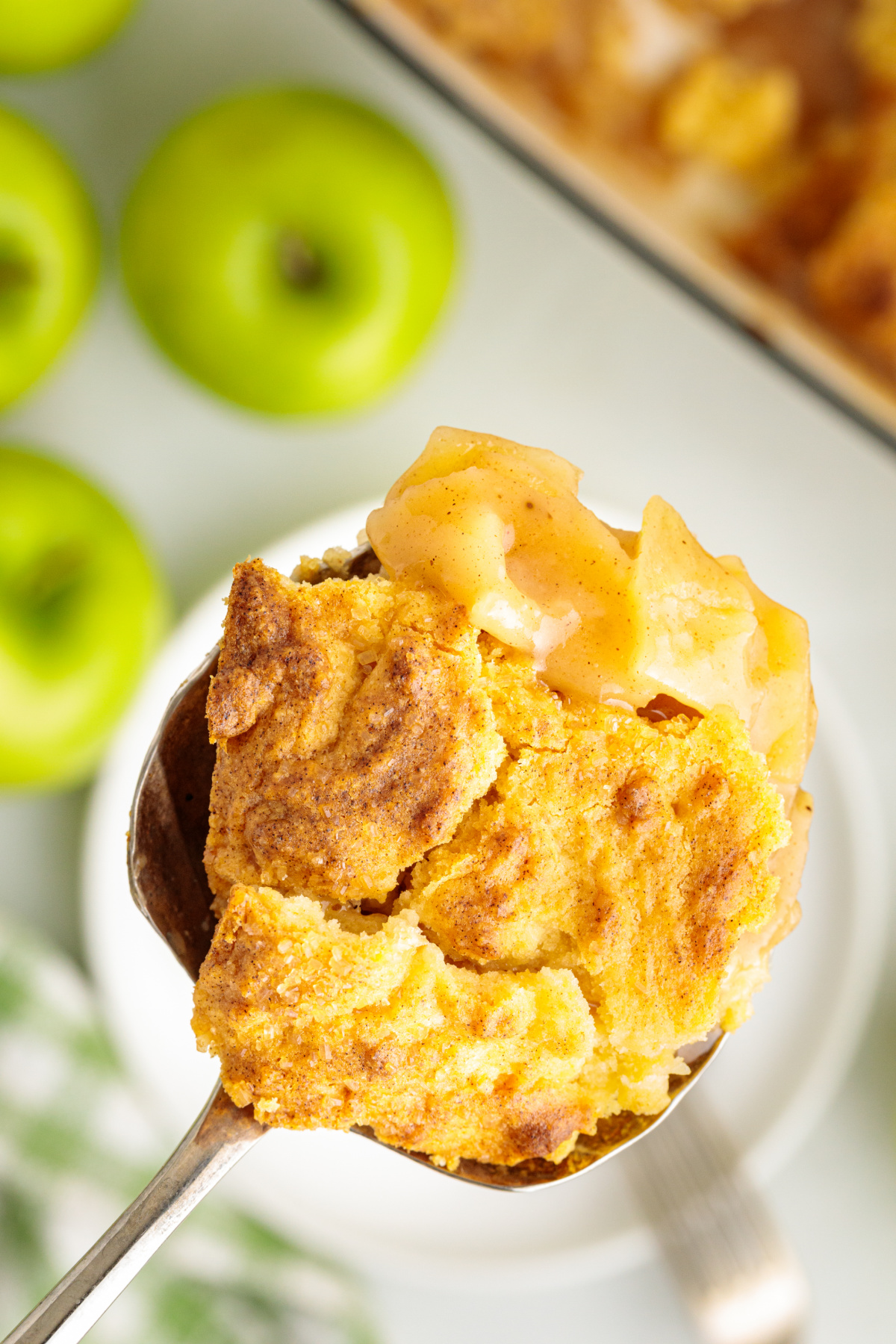 A close look at the soft golden cake topping and saucy cinnamon apple filling underneath. Spoonful of apple cake cobbler showing soft butter cake topping and cinnamon-spiced Granny Smith apple filling.