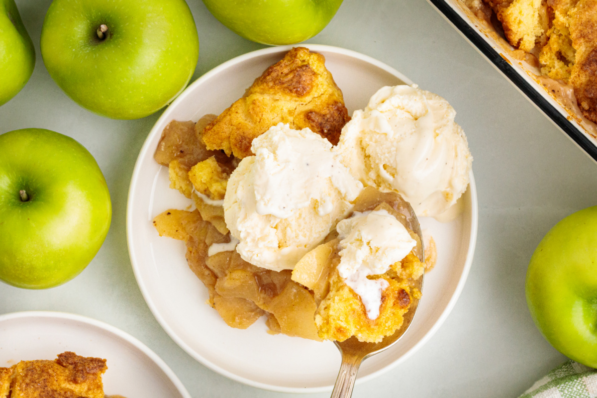 Warm cinnamon apple cobbler topped with scoops of melting vanilla ice cream. Granny Smith apples, flour, butter, sugars, eggs, cinnamon and other ingredients for apple cobbler with cake topping.