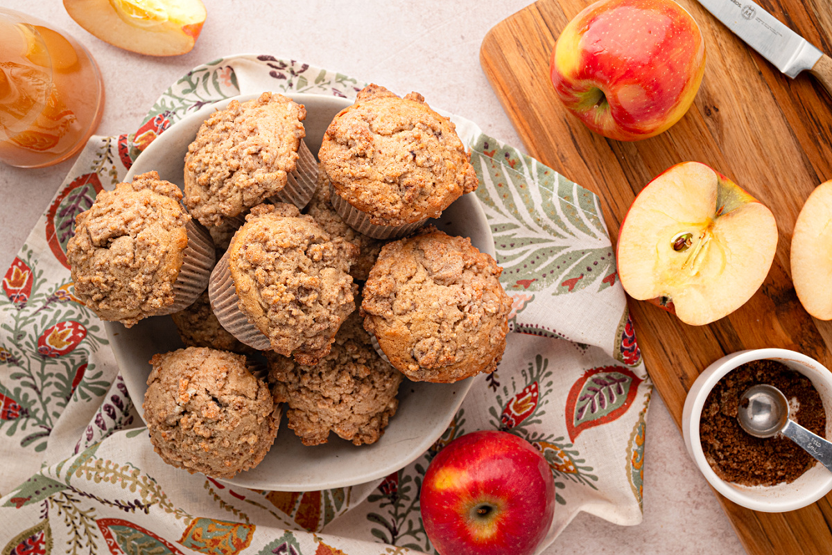 Apple cider streusel muffins made with reduced fresh apple cider and topped with buttery cinnamon streusel. Apple cider streusel muffins on a plate with fresh apples, apple cider and brown sugar cinnamon nearby.