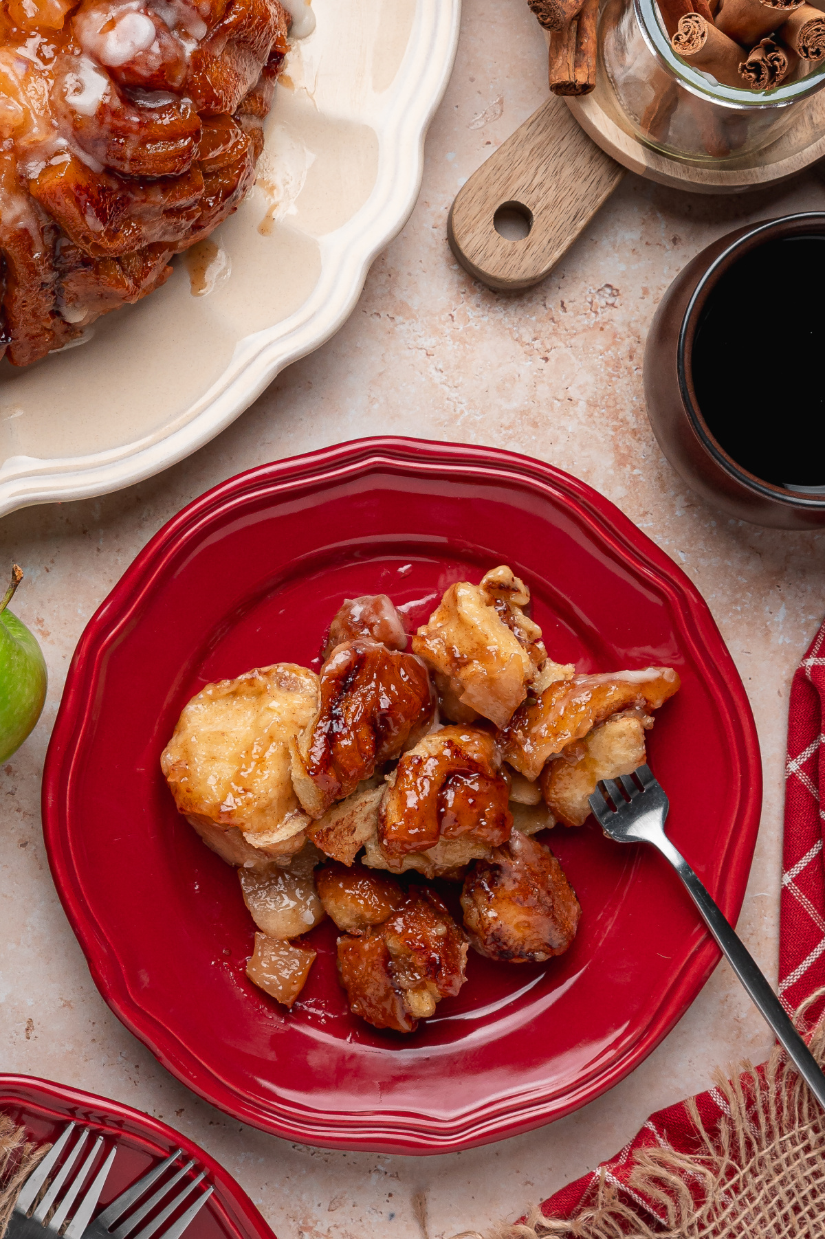 Warm cinnamon roll monkey bread pieces with apple pie filling and brown sugar sauce served on a red plate.