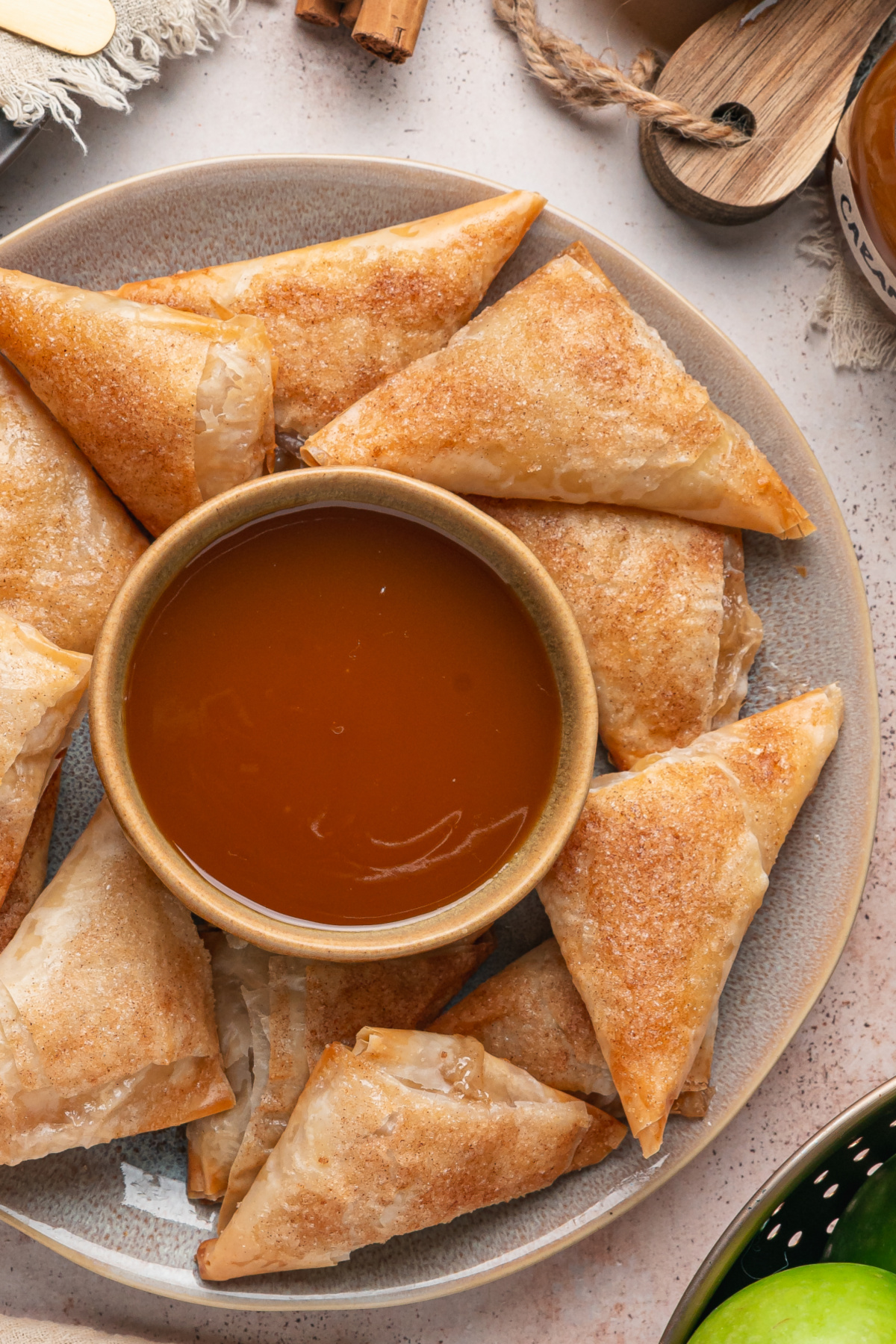 Apple Pie Samosas with Caramel Sauce Apple pie samosas made with phyllo dough and cinnamon sugar arranged around a bowl of caramel sauce.