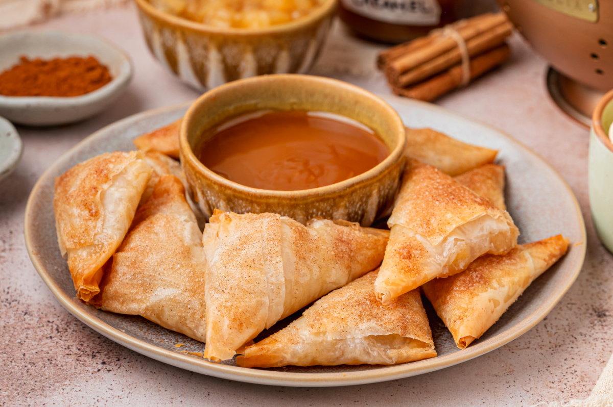 Cinnamon Sugar Apple Pie Samosas Cinnamon sugar apple pie samosas arranged on a plate with caramel sauce for dipping.
