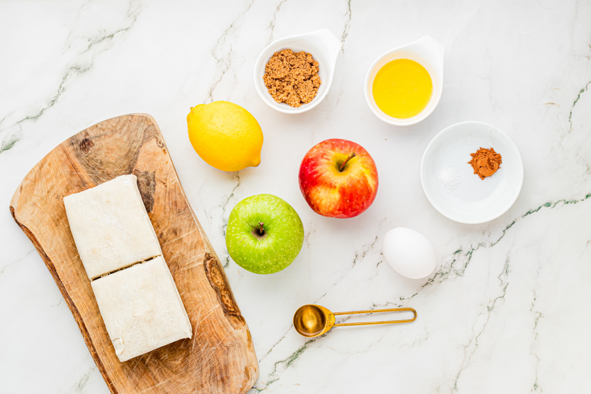 Ingredients for making an apple tart with puff pastry and fresh apples Puff pastry, Granny Smith and Dazzle apples, lemon, brown sugar, butter, egg, cinnamon and salt