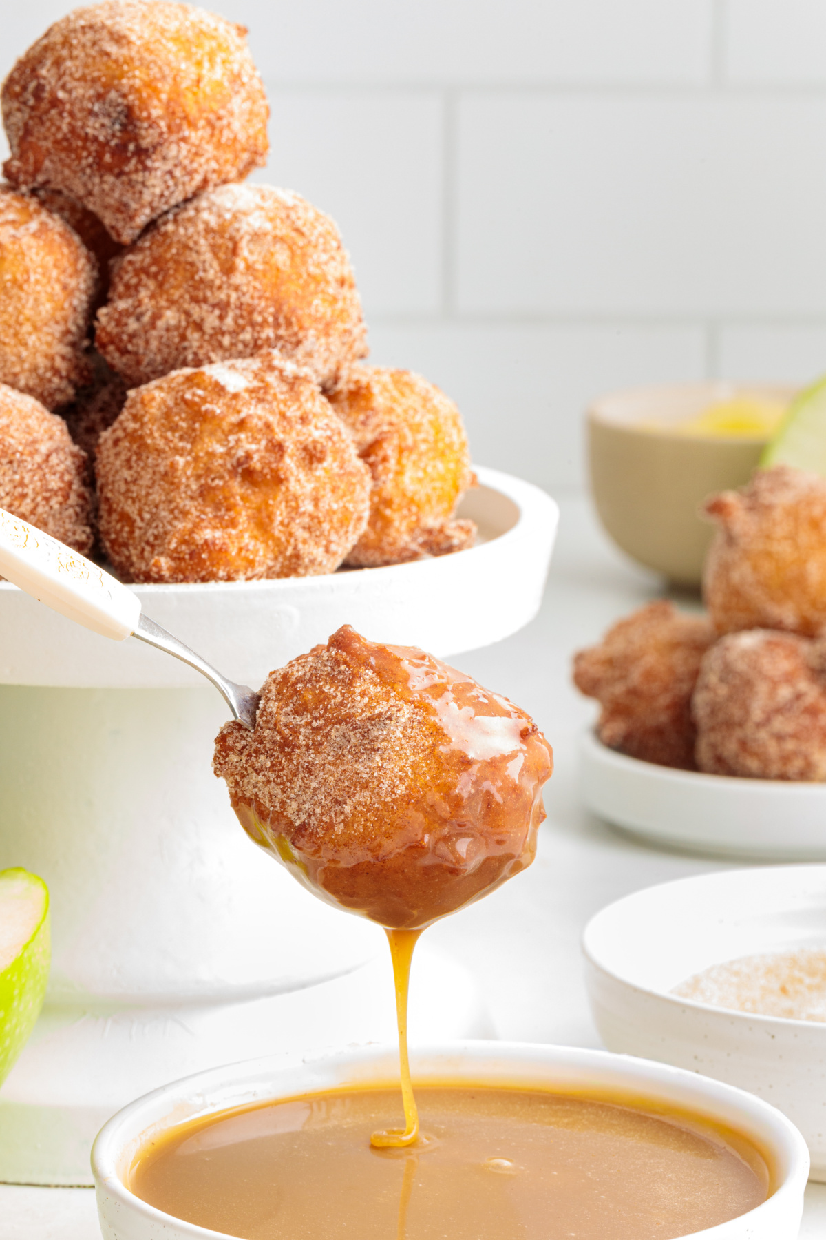 Warm applesauce fritter dripping with maple caramel sauce Cinnamon sugar applesauce fritter dipped in maple caramel with more fritters in the background