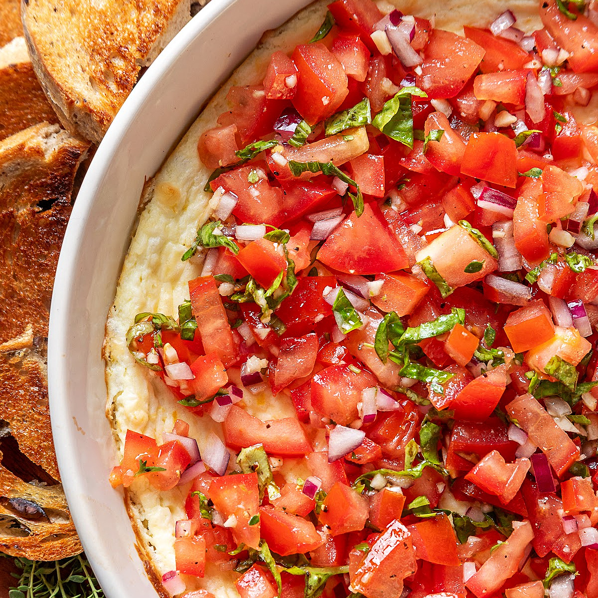 Baked feta bruschetta dip topped with fresh Roma tomatoes, red onion, basil and thyme, served with toasted bread.