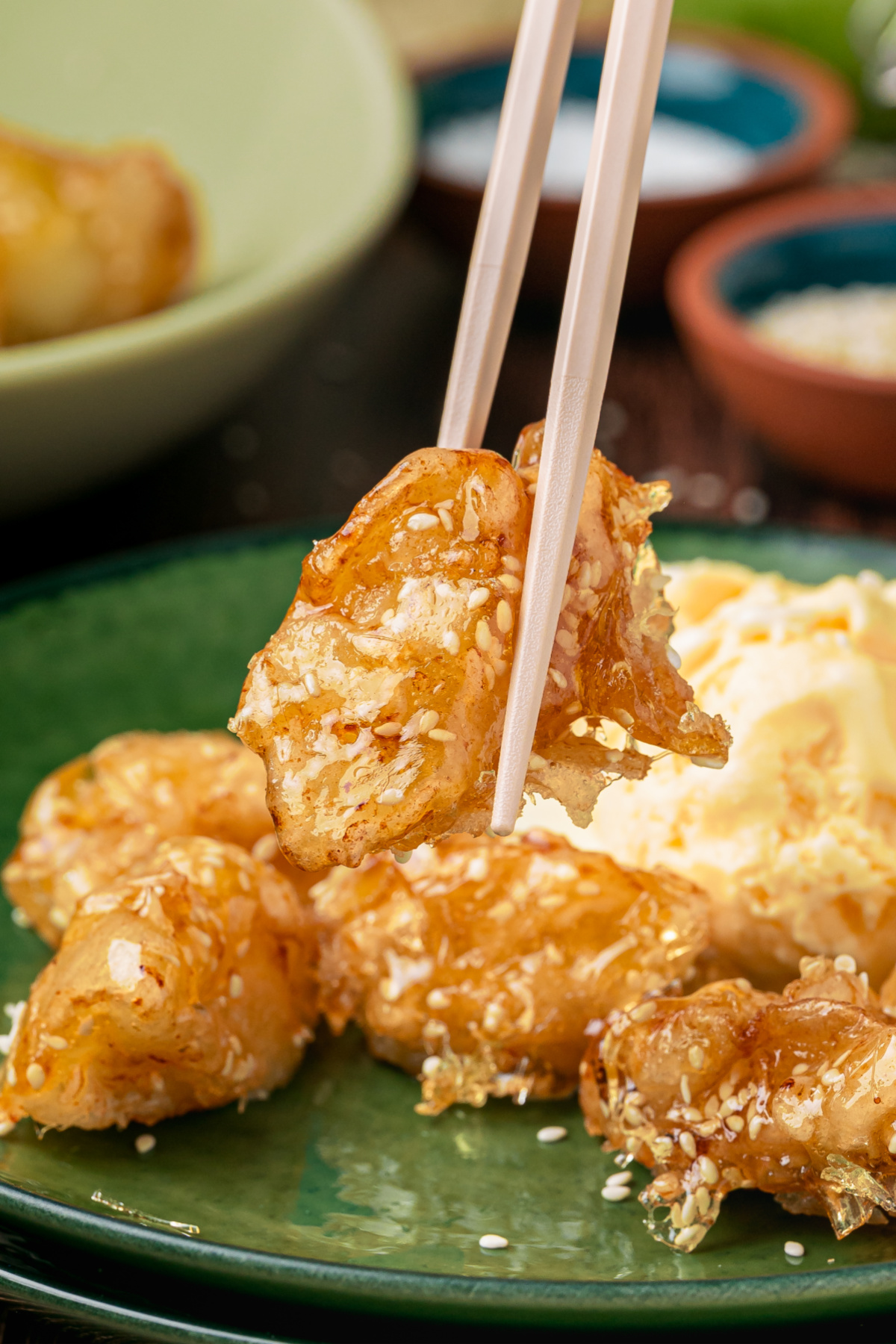 Chinese Toffee Apples with Crisp Caramel Shell Chinese toffee apples with sesame caramel held with chopsticks over a serving plate