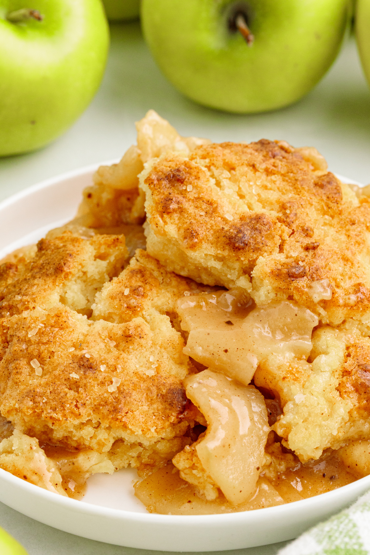 Tender Granny Smith apples with cinnamon sauce and pieces of golden butter cake topping. Cinnamon-spiced Granny Smith apple filling beneath pieces of soft golden butter cake topping with coarse sugar.