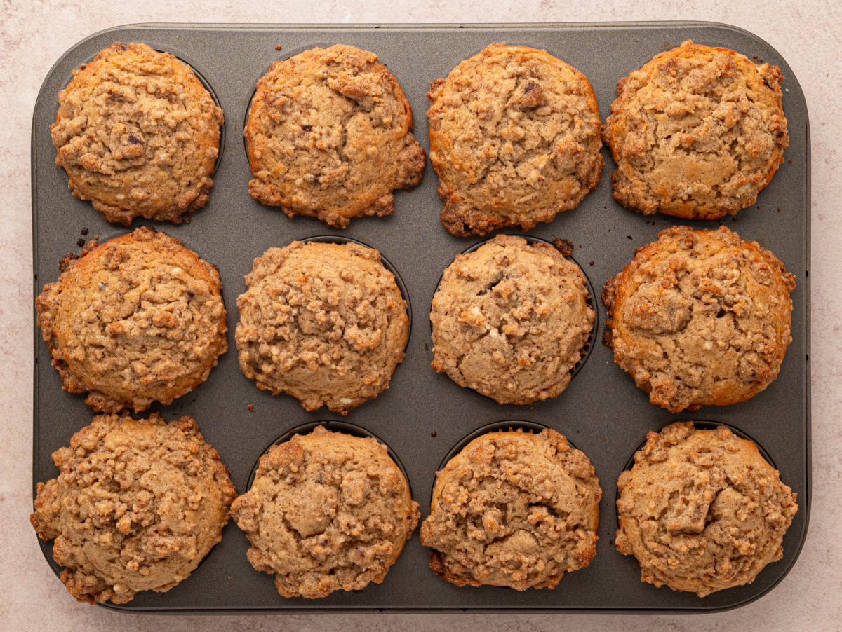 Freshly baked cider-spiced muffins covered with large pieces of buttery cinnamon streusel. Freshly baked cinnamon streusel muffins with tall tops in a 12-cup muffin pan.