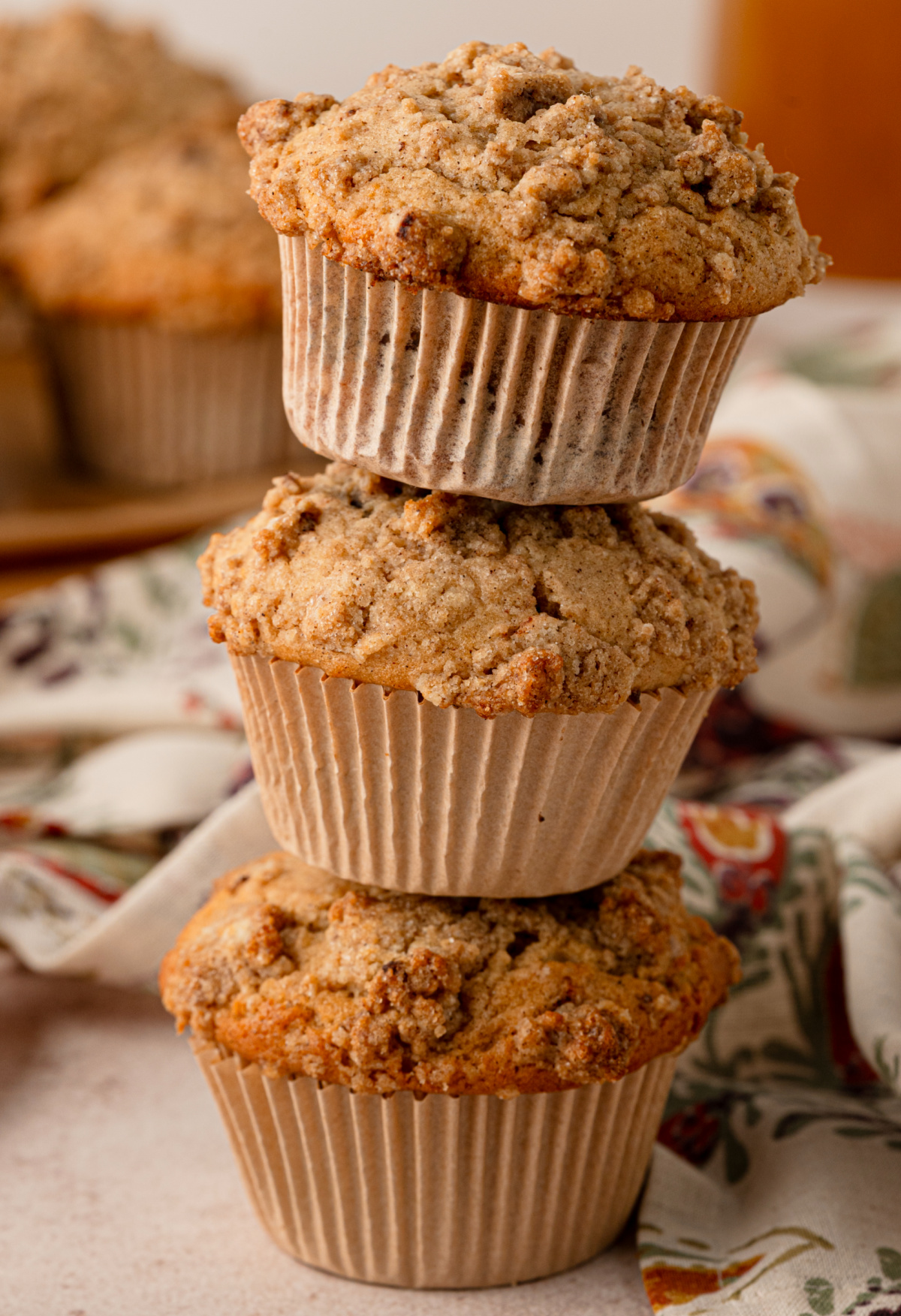 Cider-spiced muffins with tall tops and large pieces of buttery cinnamon streusel. Three cider-spiced muffins stacked to show their tall tops and cinnamon streusel topping.