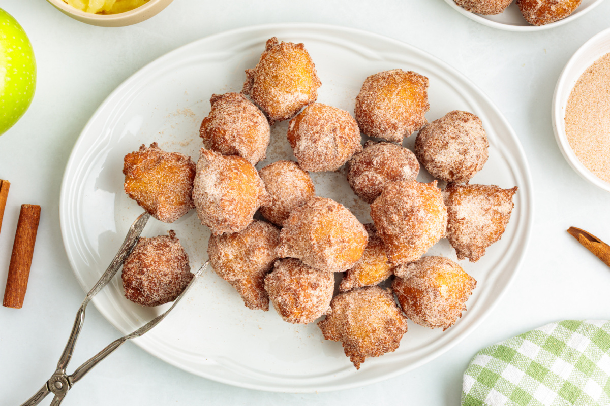 Freshly fried applesauce fritters coated in cinnamon sugar Cinnamon sugar applesauce fritters piled on a white serving platter