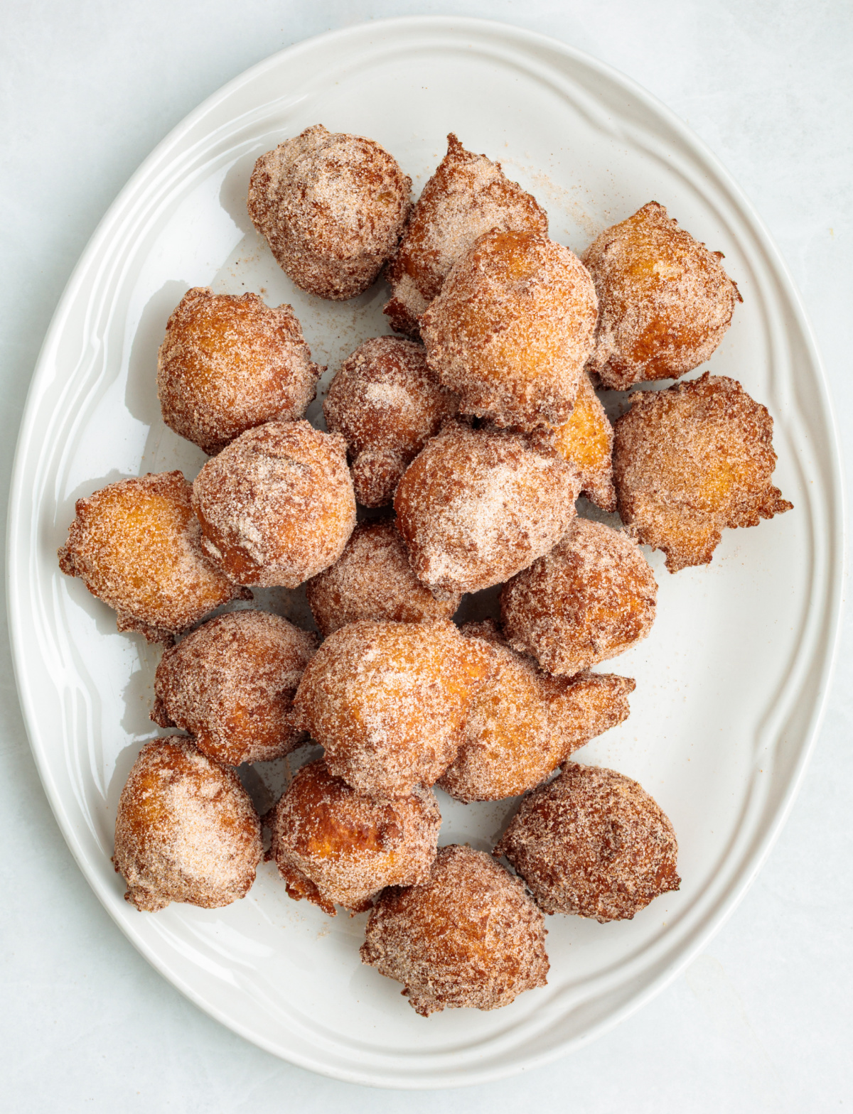 Cinnamon sugar coated applesauce fritters after frying Fried applesauce fritters coated in cinnamon sugar on a white platter