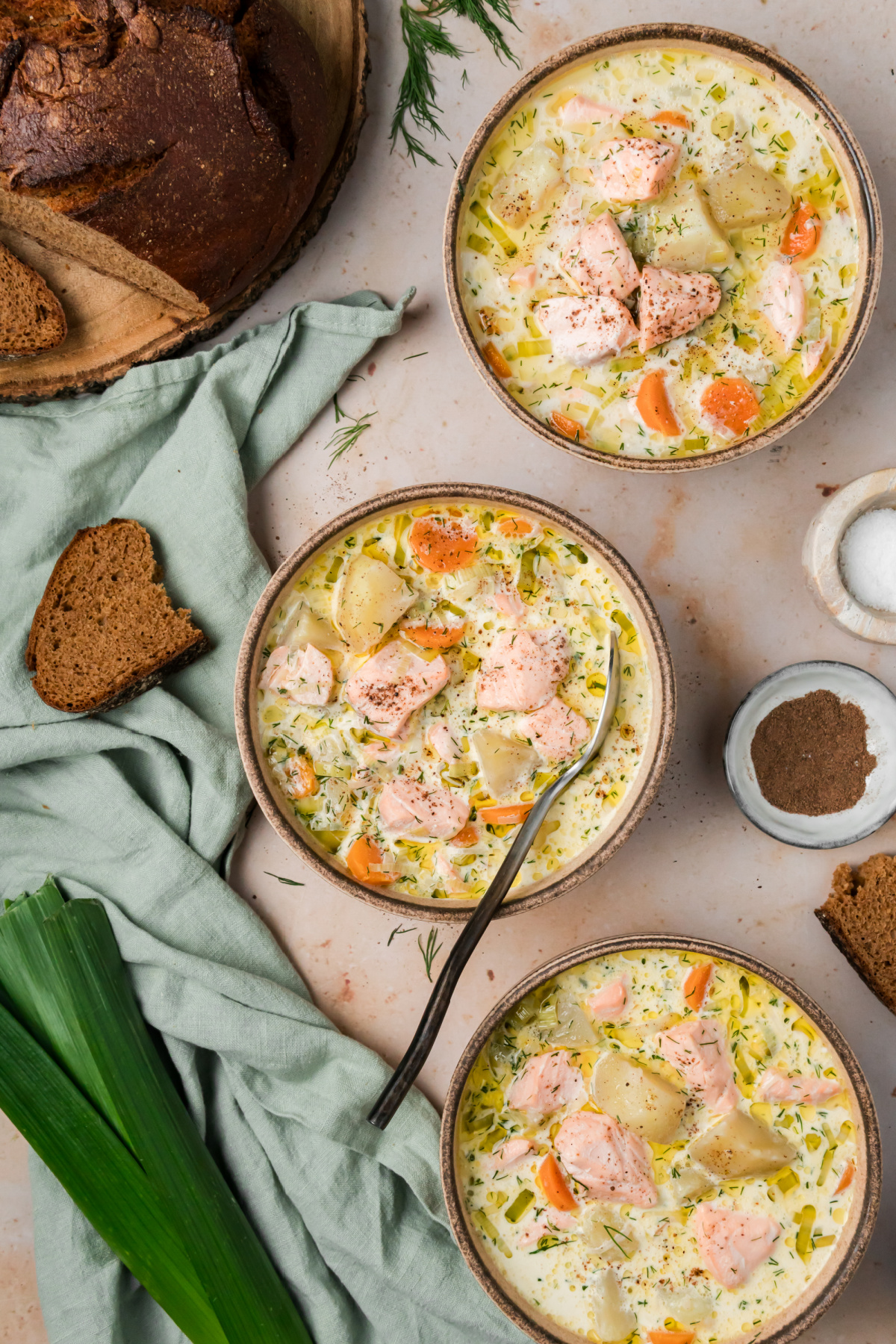 Three bowls of Finnish salmon soup with salmon, potatoes, carrots, leeks and fresh dill served with dark bread.