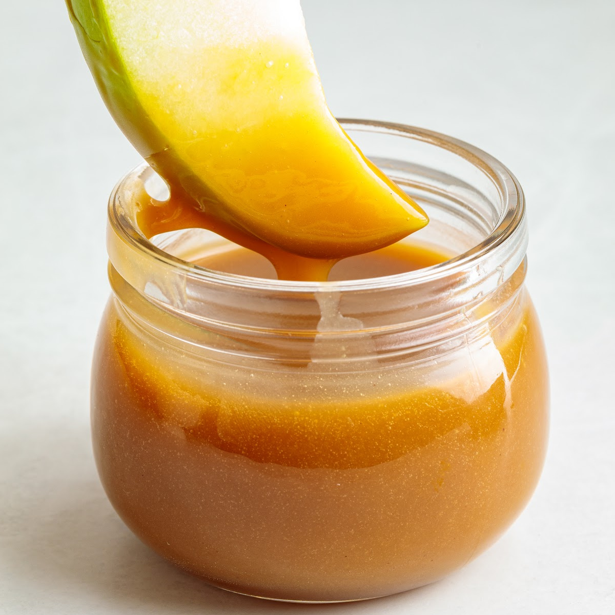 Granny Smith apple slice dipped into maple caramel dip in a glass jar