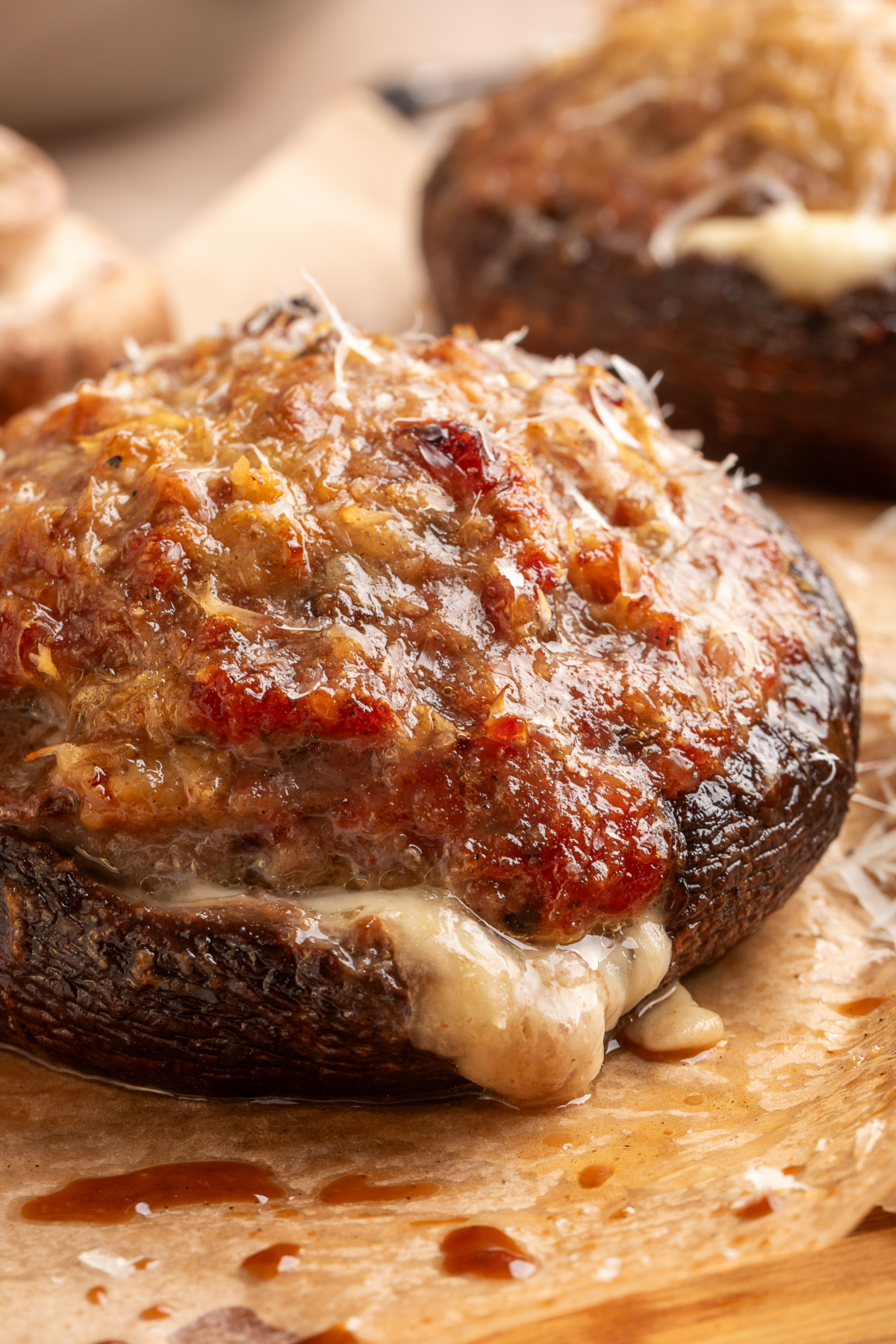 Close-up of a grilled portobello stuffed with sweet Italian sausage, with Parmesan on top and mozzarella melting underneath. Italian sausage stuffed portobello mushroom topped with browned Parmesan and melted mozzarella